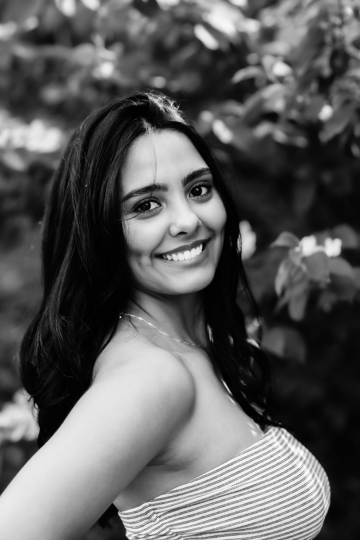 Black and white portrait showing a joyful smile against a soft bokeh background of leaves.