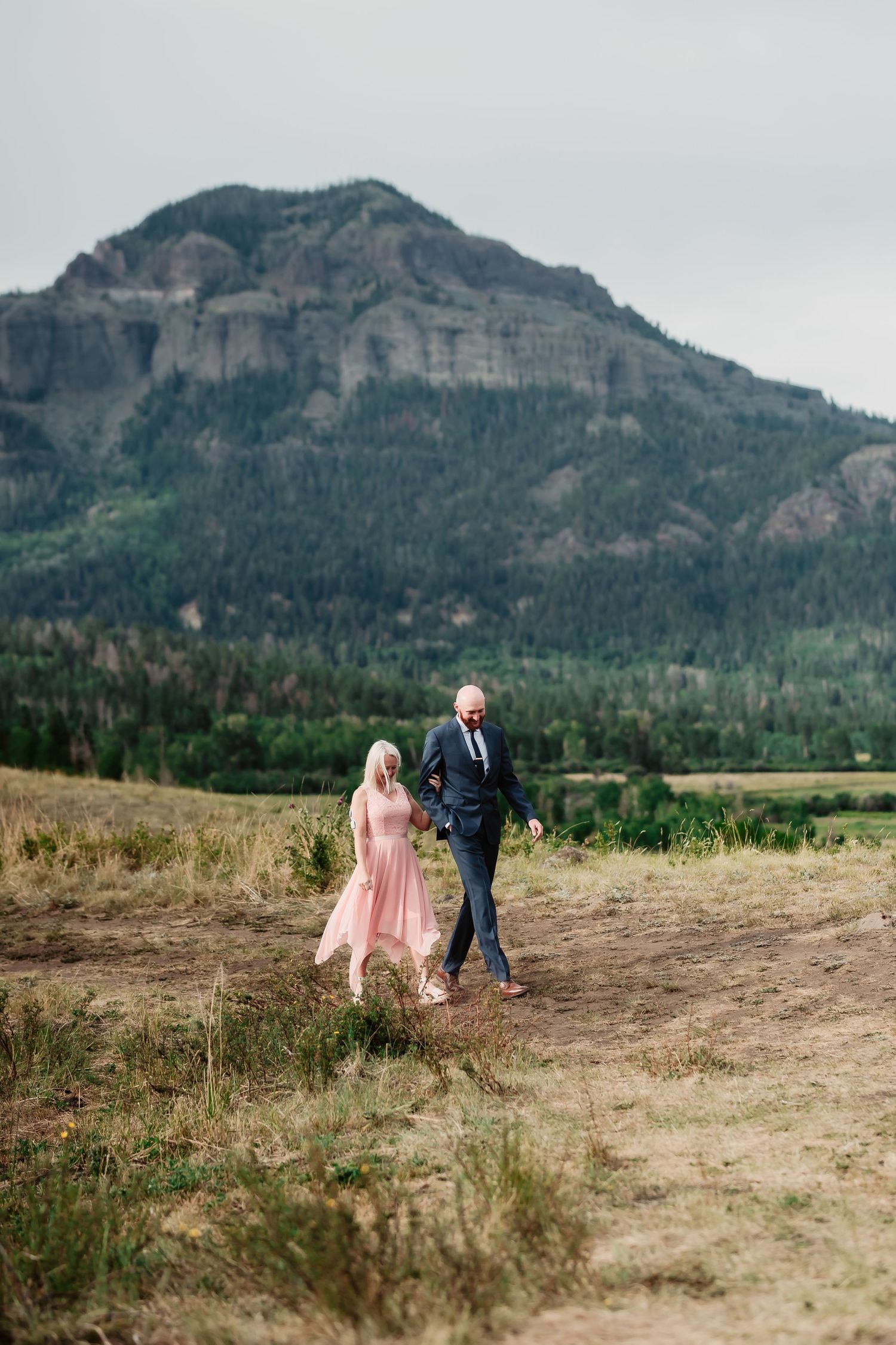 Couple walking together on mountain trail with dramatic rocky peak in background.