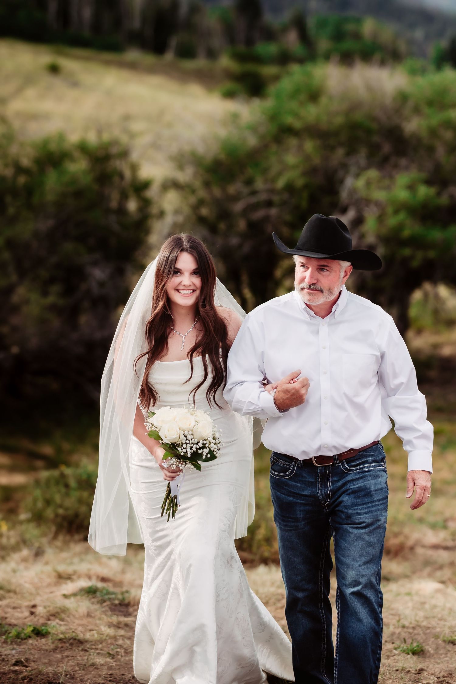 An intimate wedding moment captured outdoors with a bride in white dress alongside a western-dressed escort.