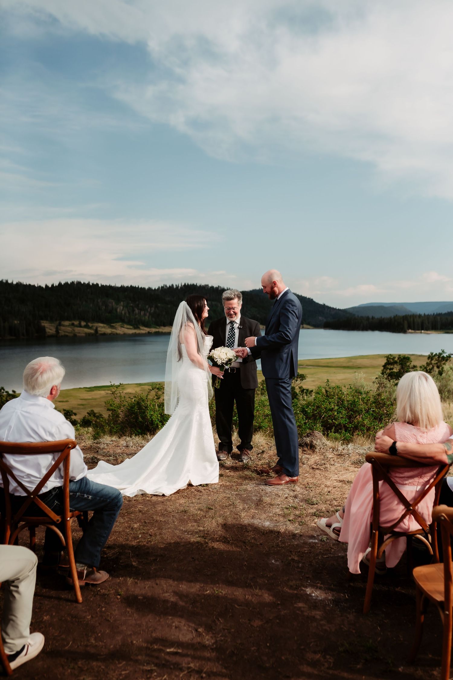 Intimate outdoor wedding ceremony by a serene lake with mountains in the background.