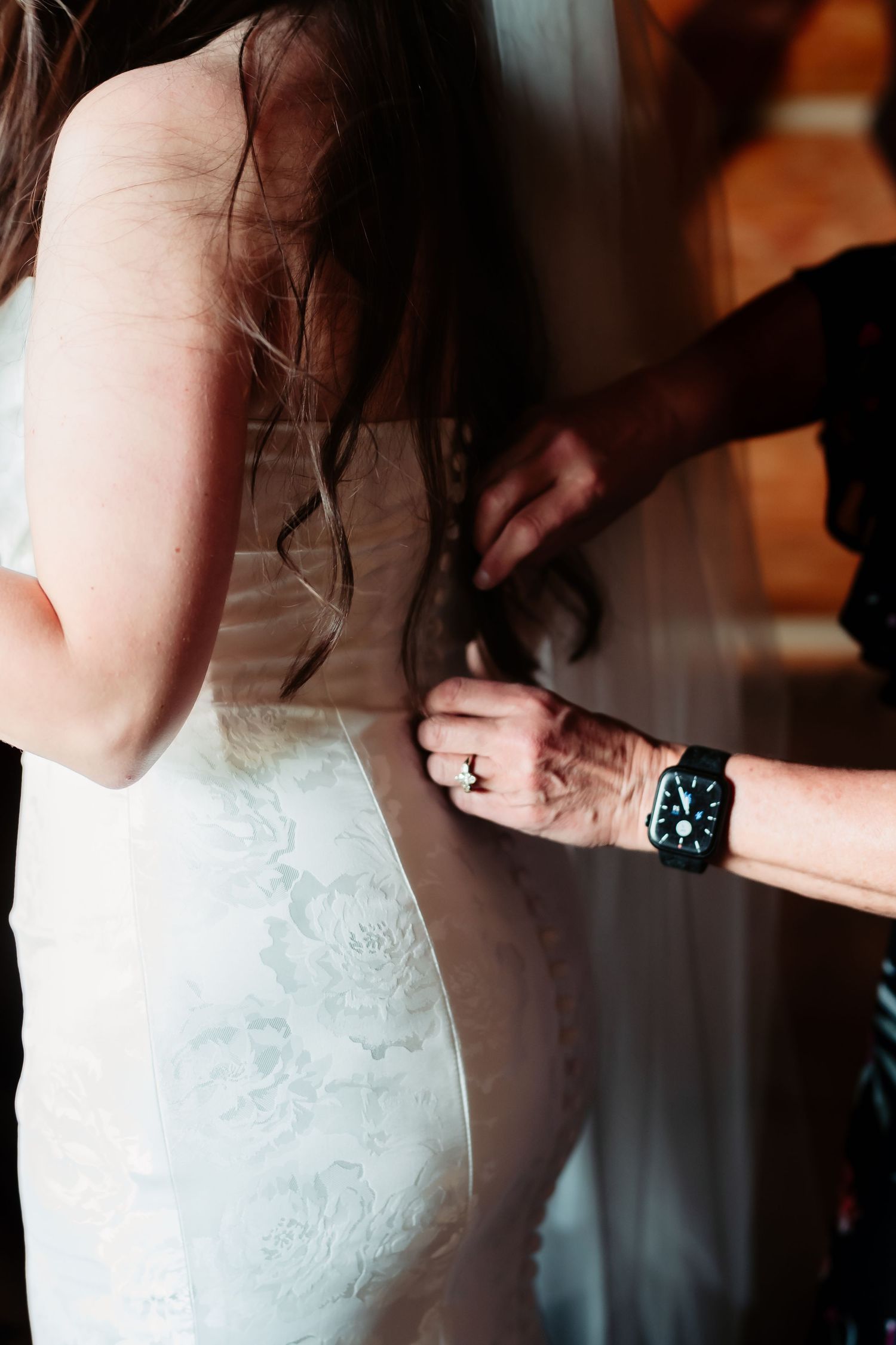 Close-up details of a bride's white lace wedding dress being buttoned up.