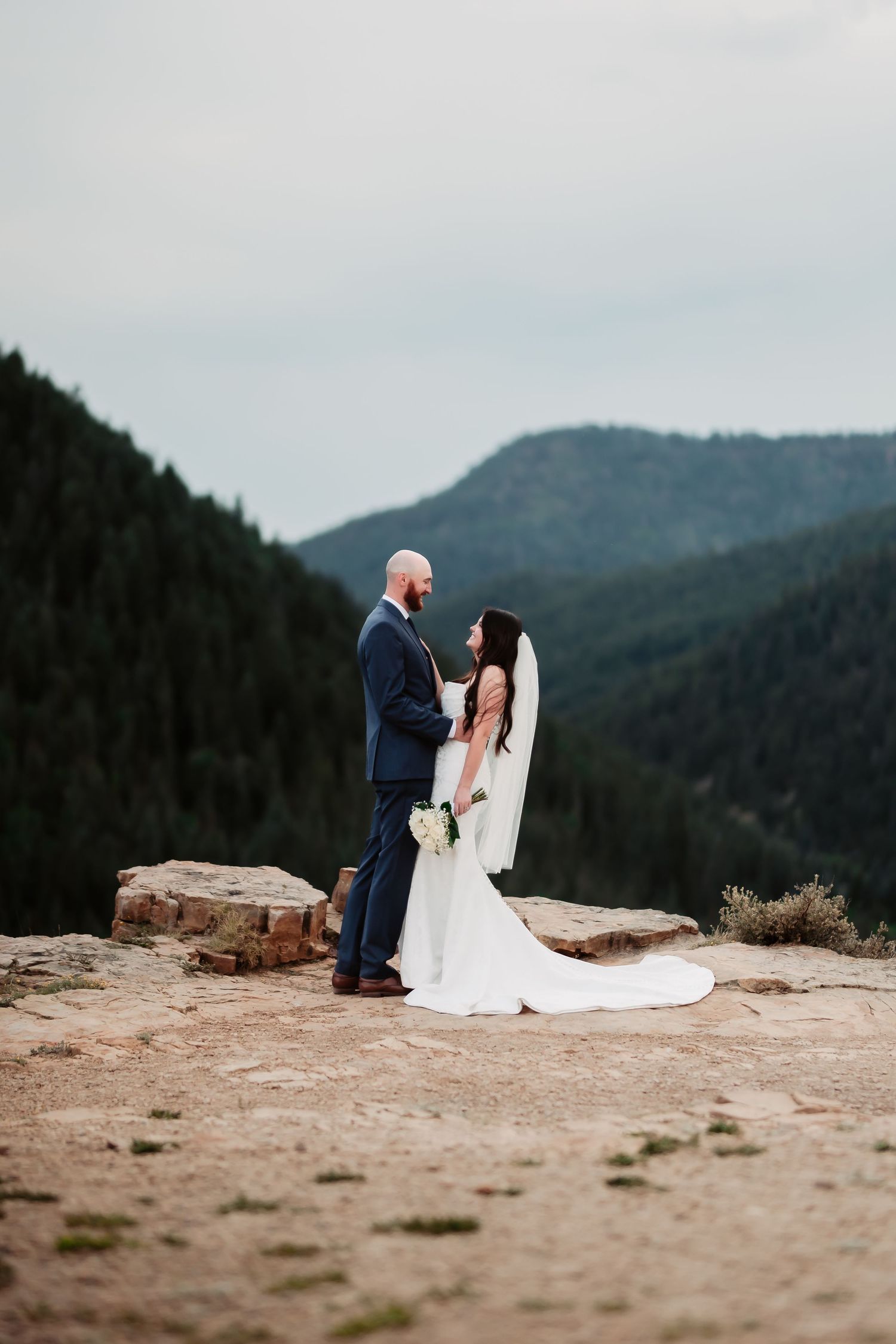 Wedding couple shares tender moment on mountain overlook with dramatic valley views.