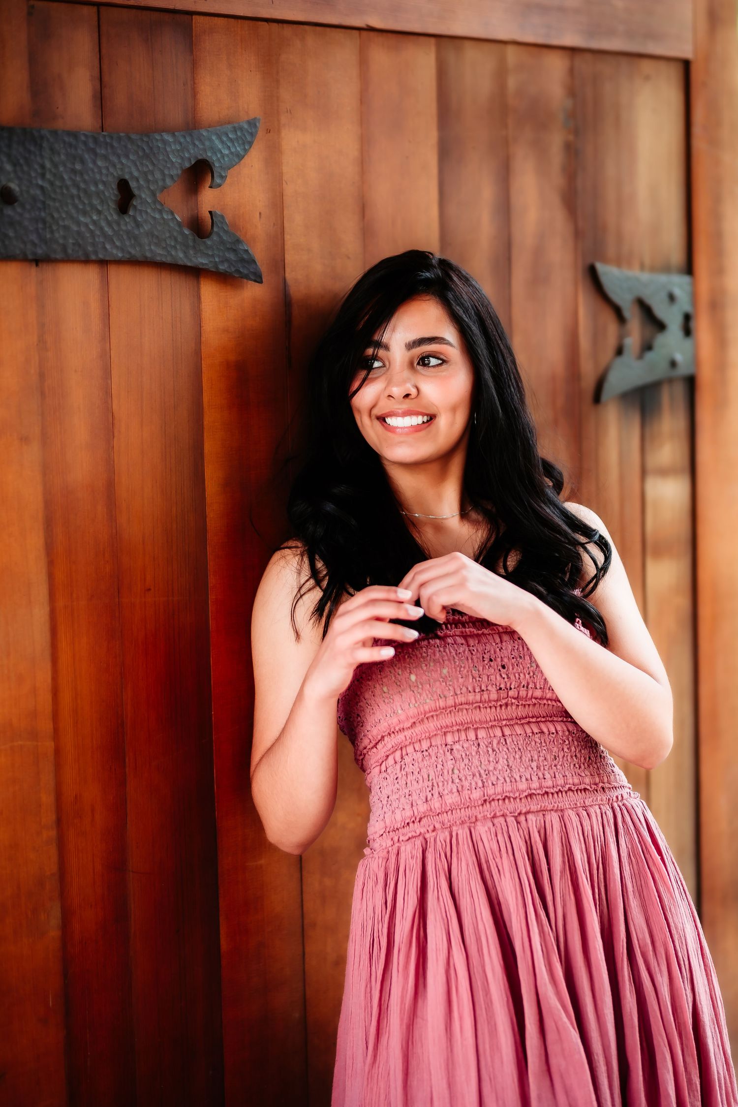 Woman in a rose-colored dress poses against a wooden wall with decorative arrows.