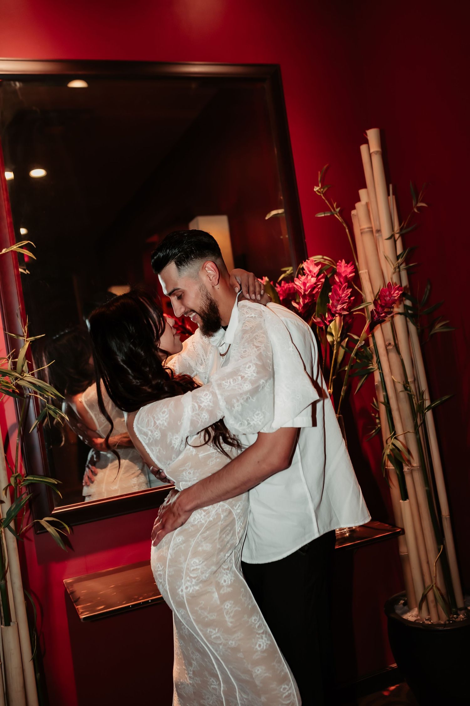 A couple shares a passionate dance in a red-lit room with floral decor.