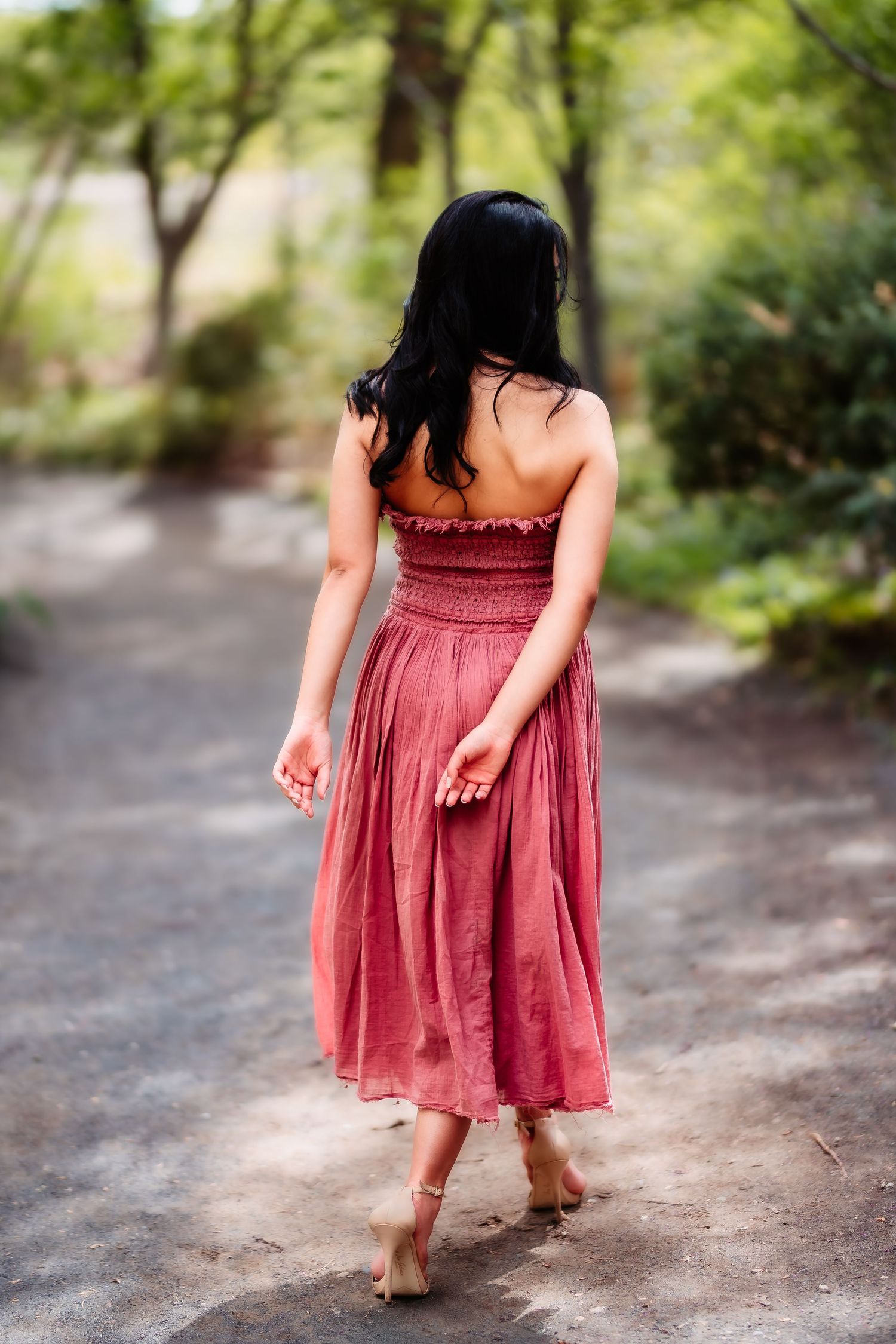 Back view of someone walking barefoot on a dirt path wearing a flowing rose-colored dress.