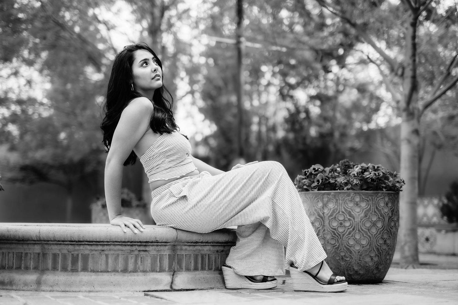 A person in light-colored clothing sits elegantly on a ledge next to a decorative planter.