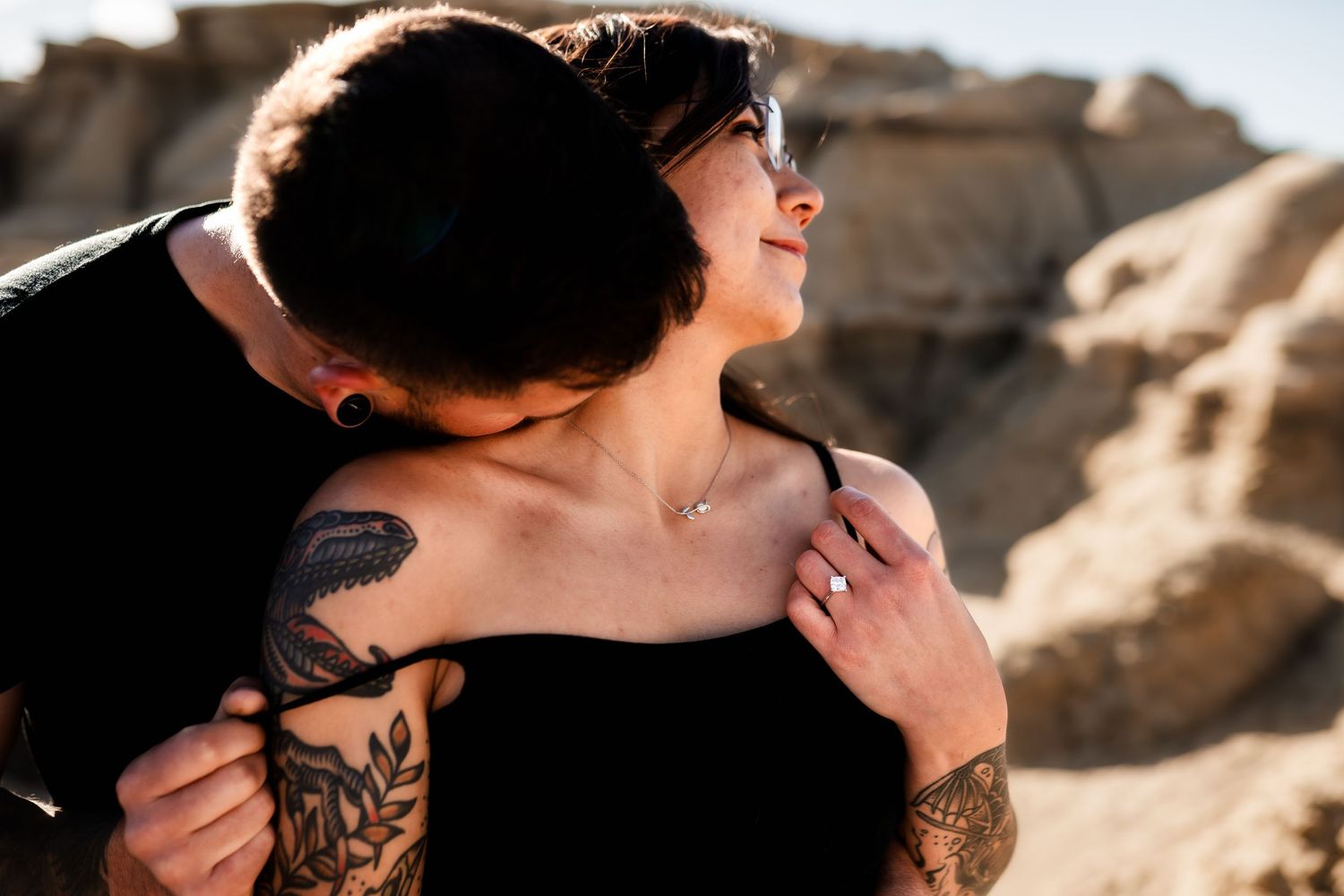 A couple embraces intimately against desert rock formations in warm sunlight.