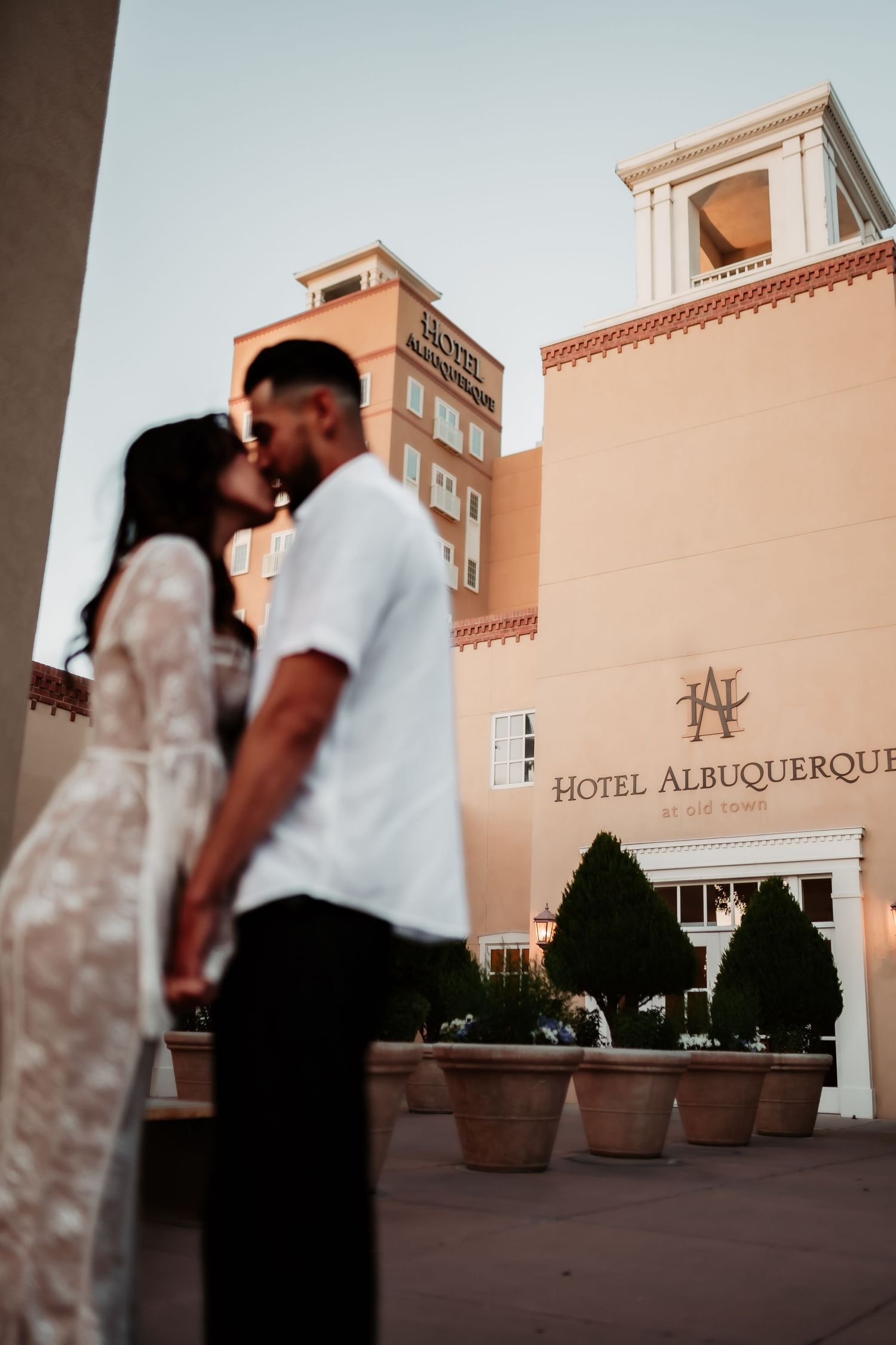 A romantic silhouette against the Hotel Albuquerque facade with terracotta-colored architecture and potted plants.