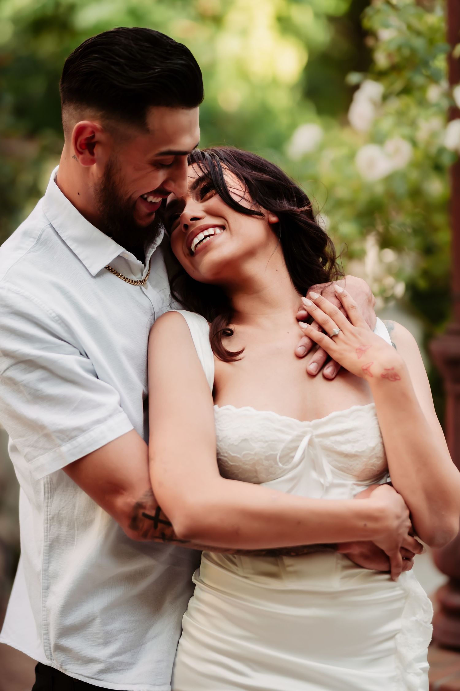 A joyful couple shares an intimate moment while embracing in a sunlit garden setting.