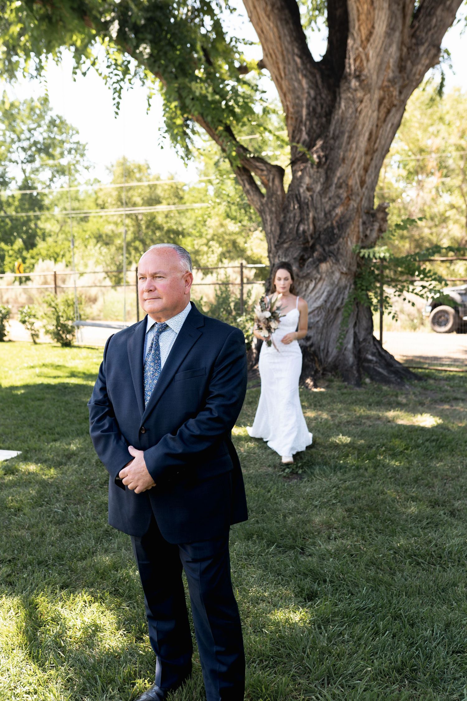 A first look moment before a wedding ceremony under a large shade tree on a sunny day.