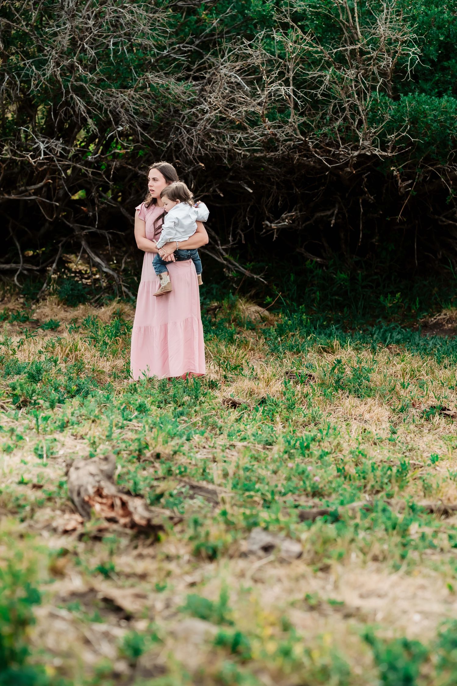A little girl in a pink dress holds a bunny in a wooded outdoor setting with lush greenery.