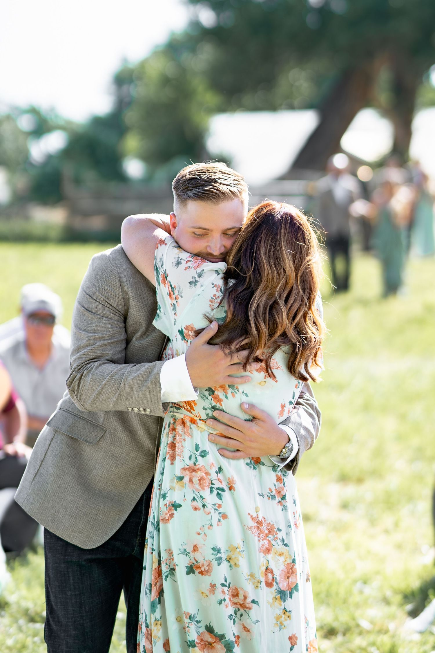 Couple embraces in sunny field during first look moment at outdoor wedding.