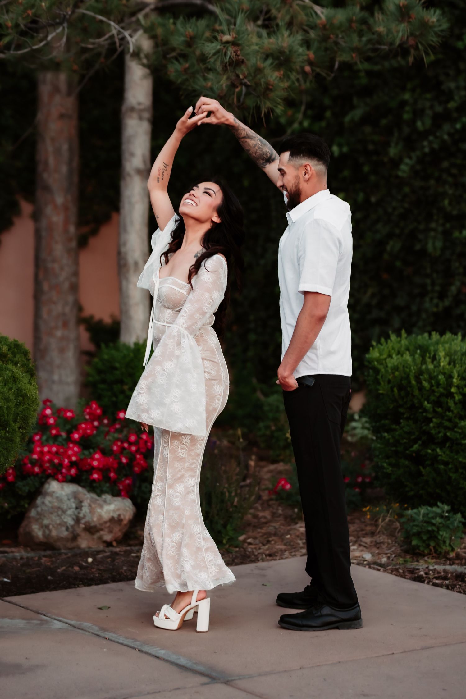 Couple in formal attire dancing outdoors with red flowers in the background.
