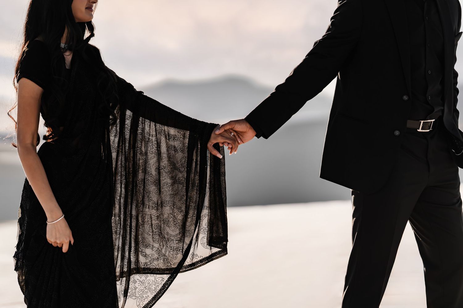 Two people holding hands while one wears flowing black fabric against a bright studio backdrop.
