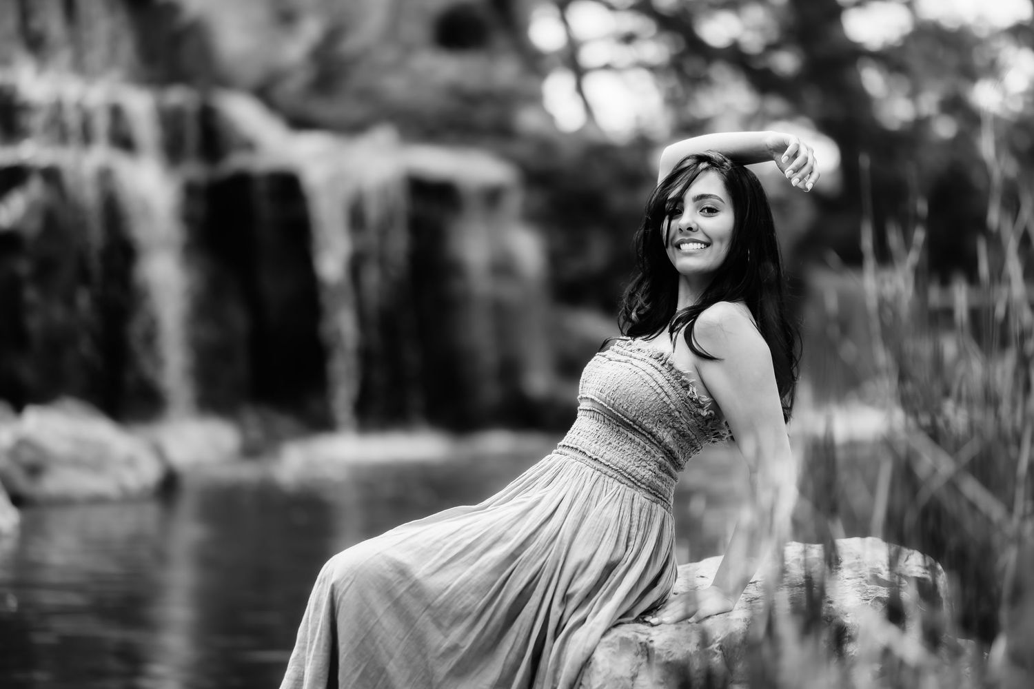 A black and white portrait by a waterfall wearing a flowing dress in an artistic pose.