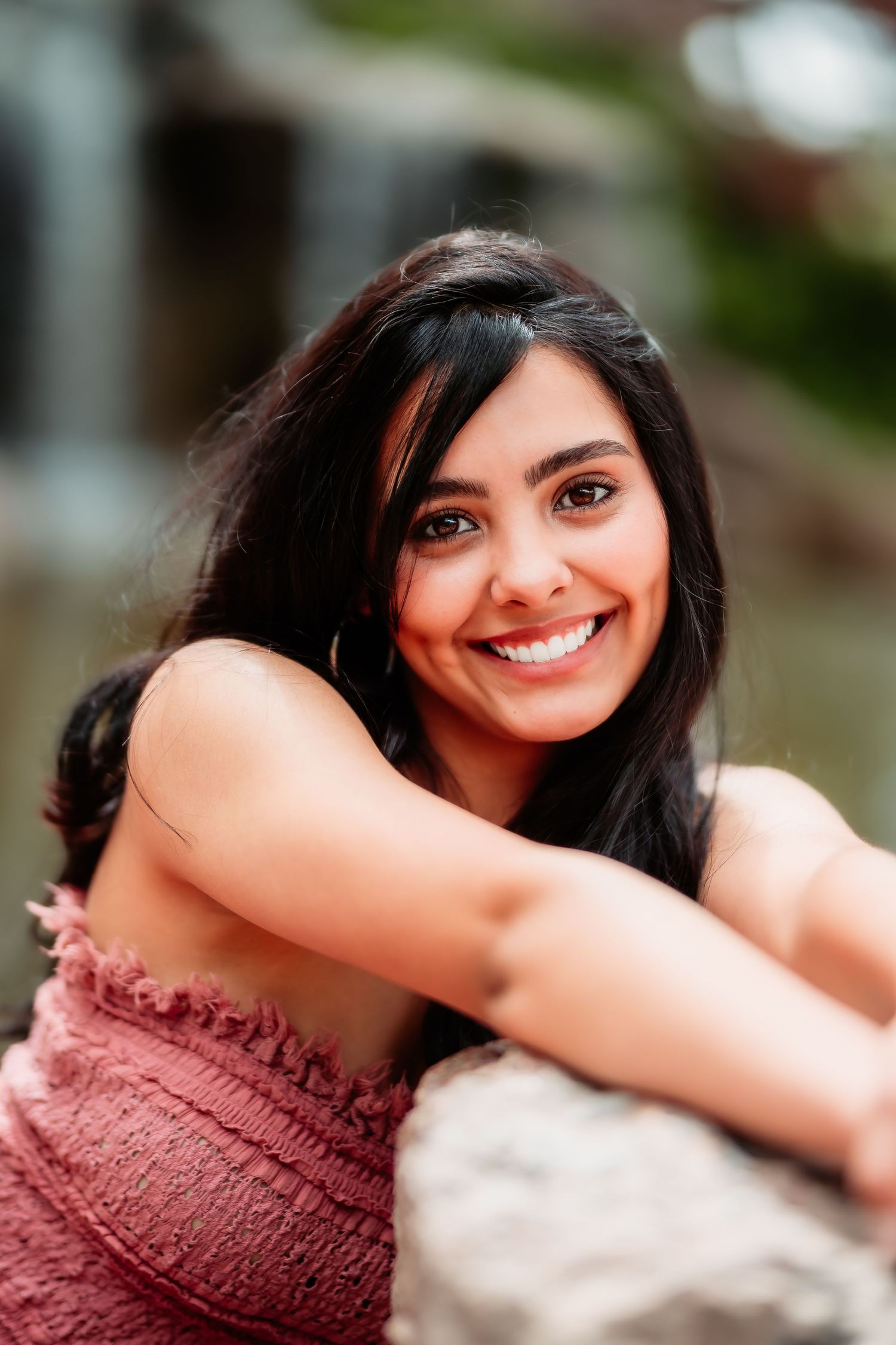 Close-up portrait showing bright smile and dark hair while wearing a pink dress outdoors.