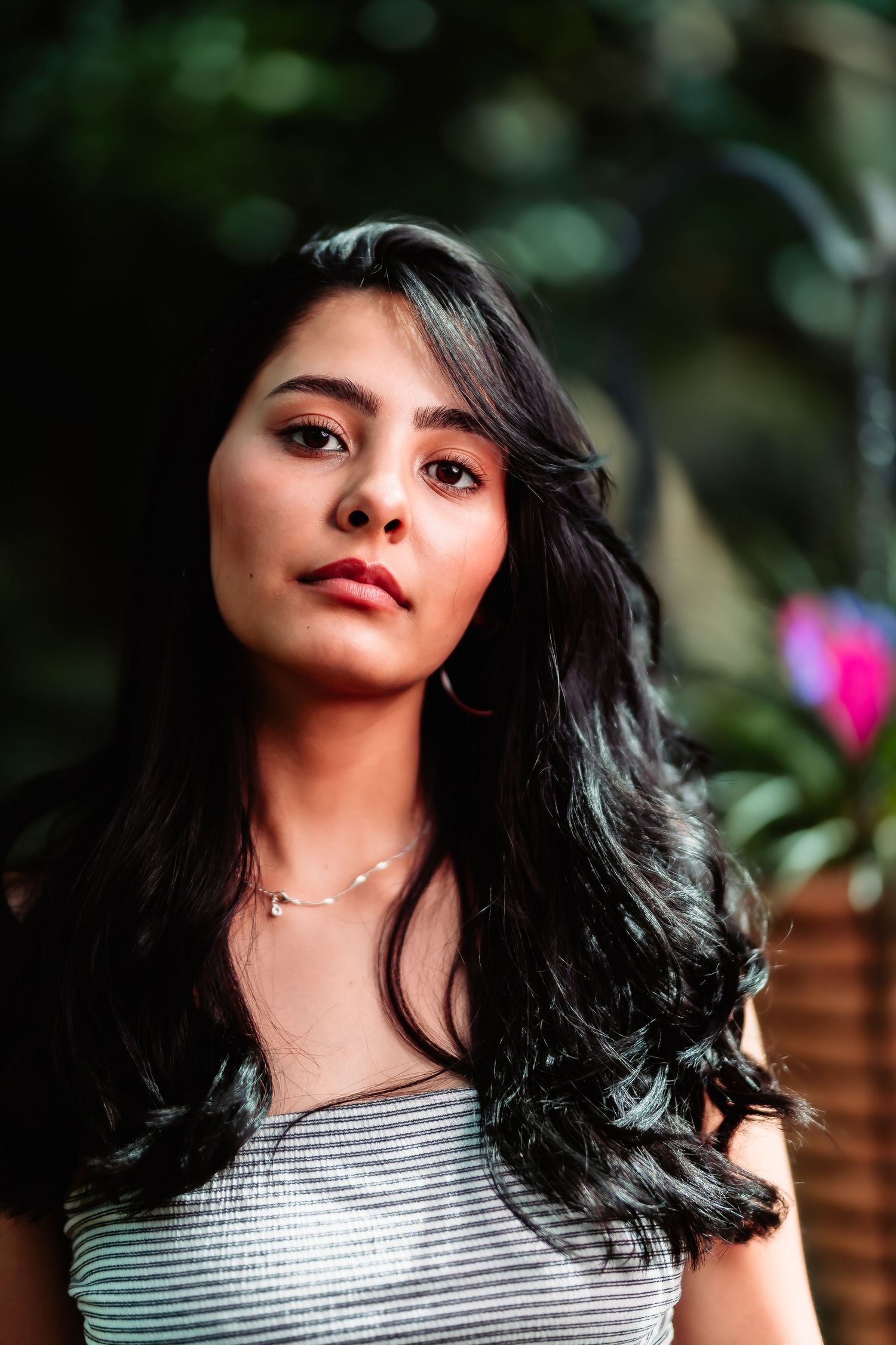 A portrait showing long dark hair and natural makeup against a blurred outdoor background.