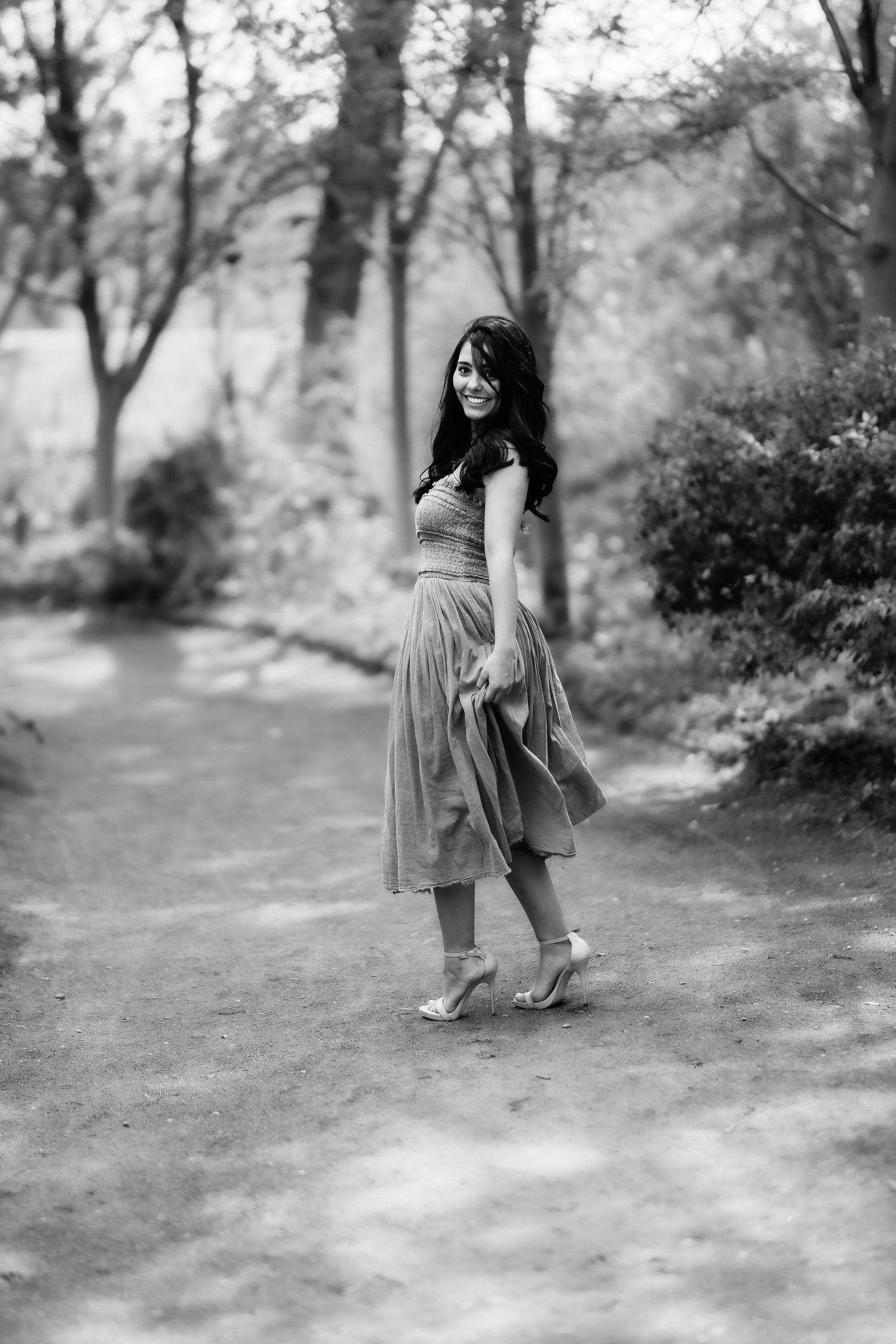 Black and white portrait of woman in flowing dress posing on wooded path in vintage style.