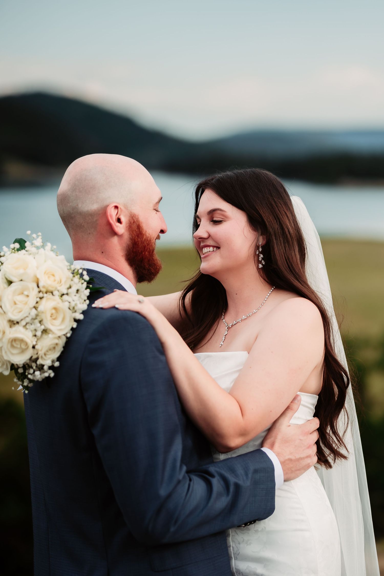 Romantic moment between newlyweds with white bouquet against mountain landscape.