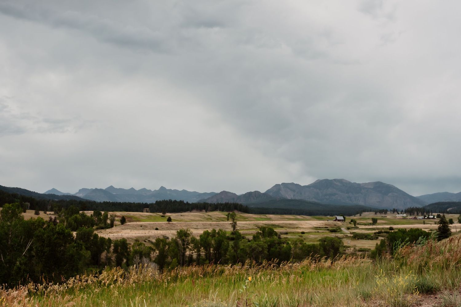 Panoramic mountain landscape view with cloudy skies and rolling grasslands.