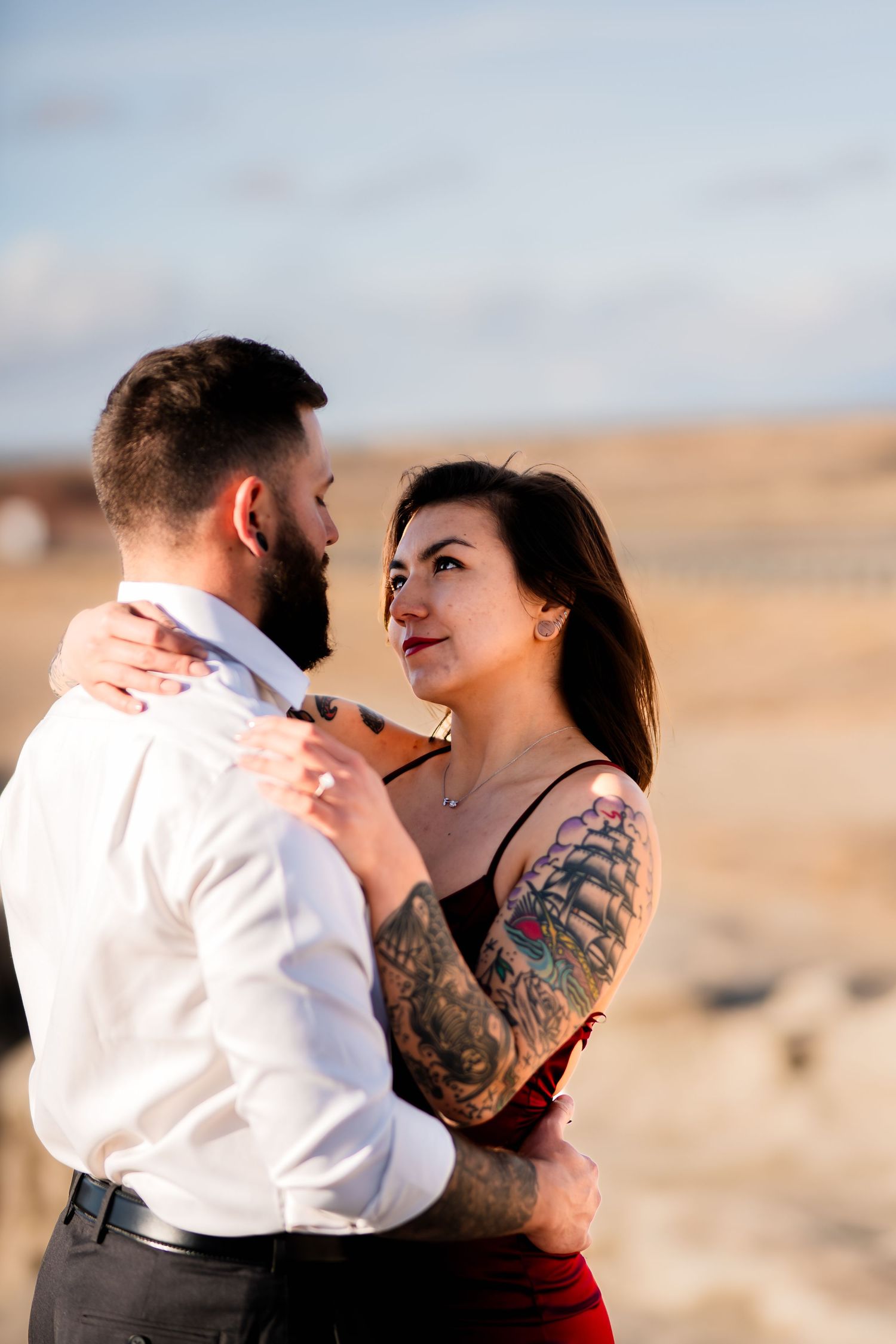A couple shares an intimate moment while dressed in formal attire against a desert backdrop.