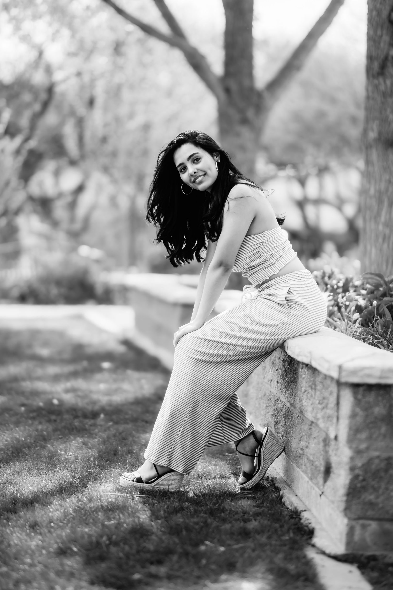 Elegant black and white portrait of a person in casual wear leaning against a stone wall outdoors.