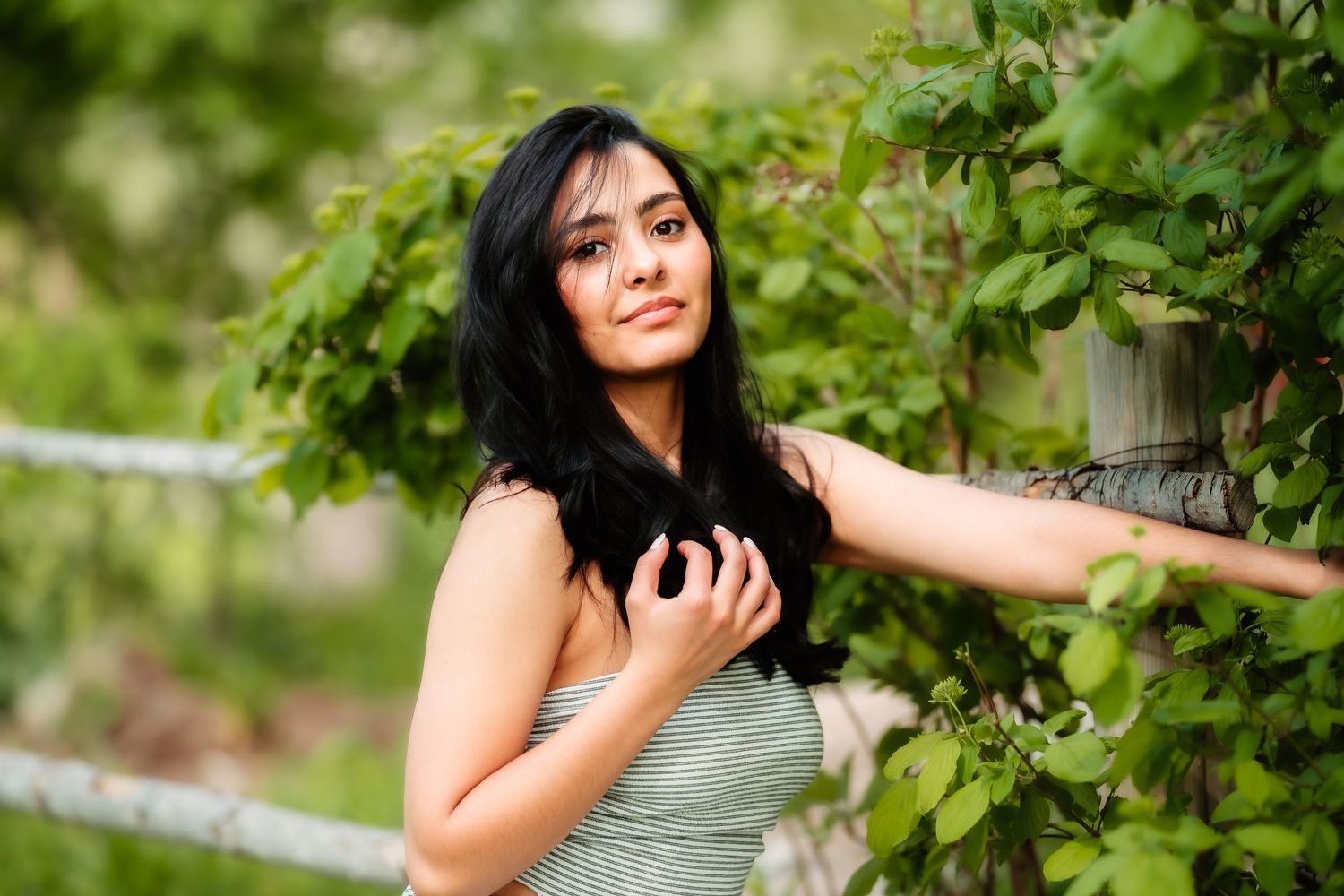 A woman in a gray dress poses gracefully among lush green vines in an outdoor garden setting.