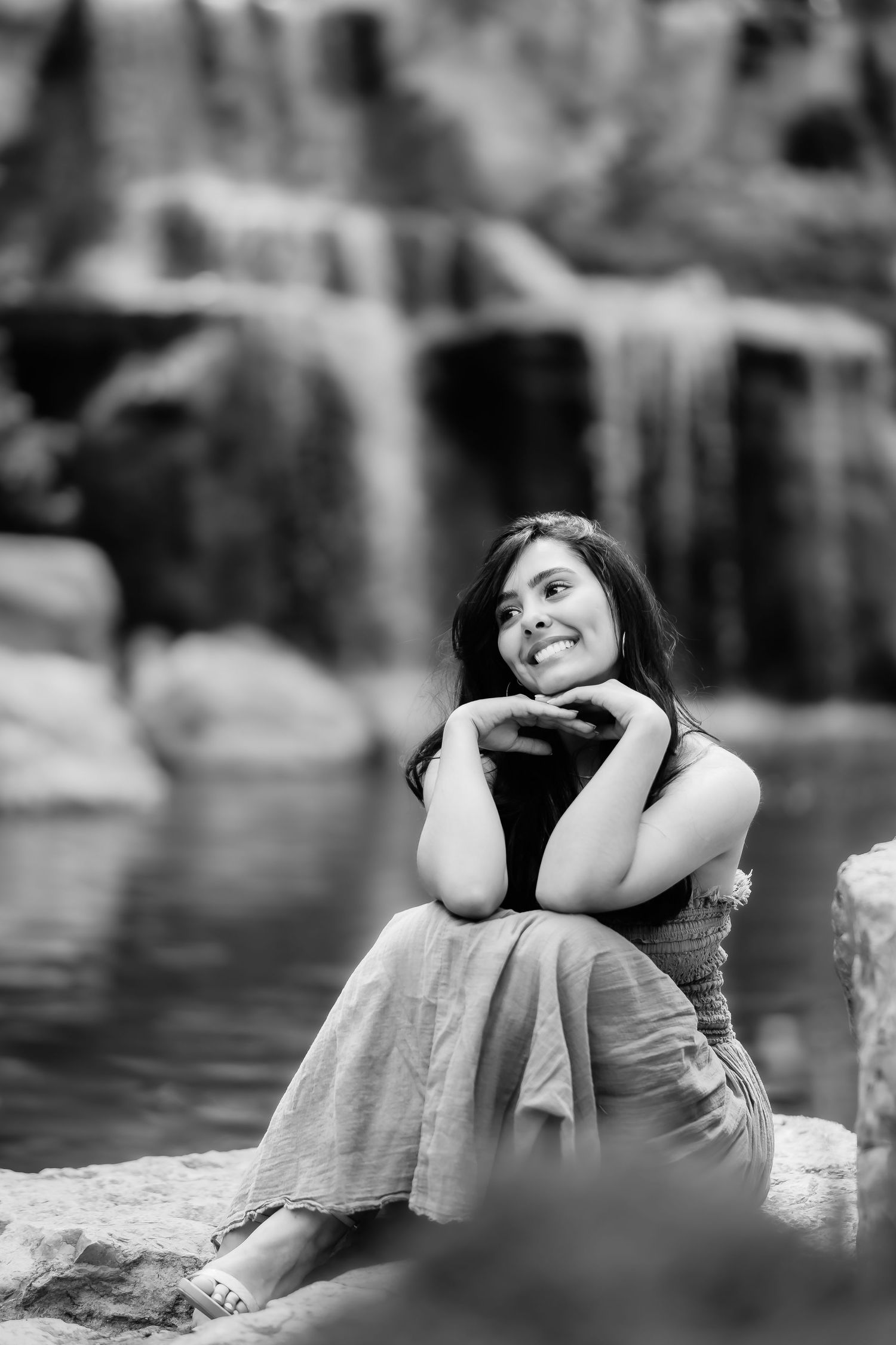 A black and white portrait of a person sitting by a waterfall in casual dress with a dreamy expression.