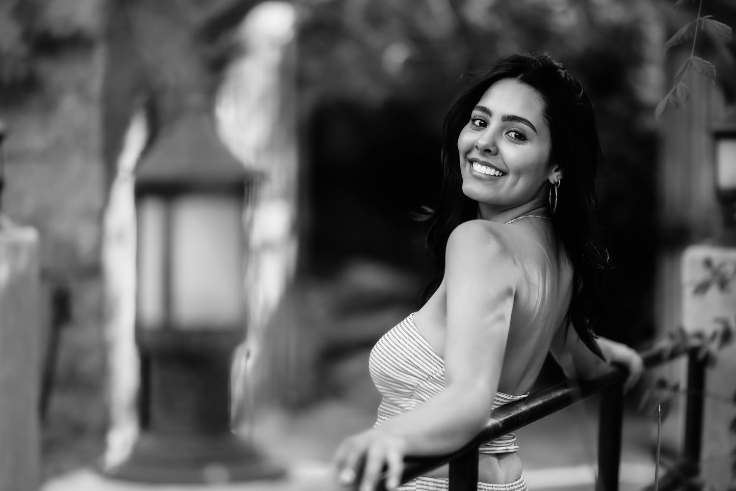 Black and white portrait of woman looking over shoulder with bright smile in outdoor setting.