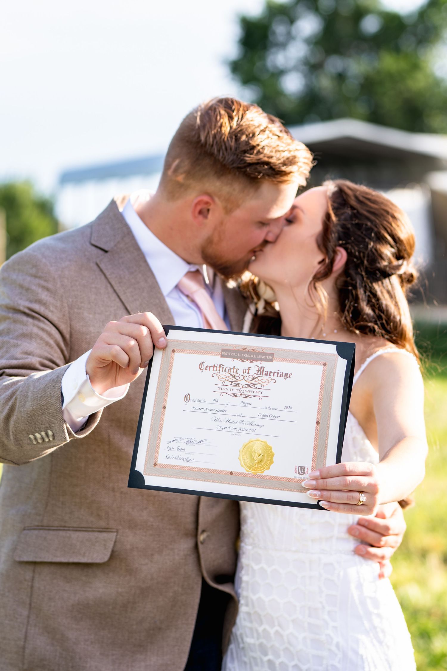 A newly married couple sharing a moment while displaying their marriage certificate in an outdoor setting.