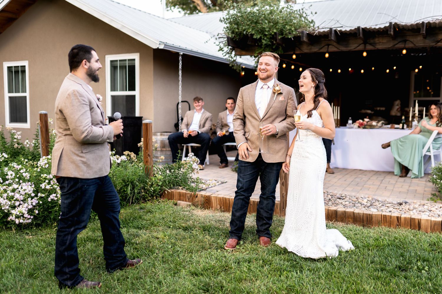 A backyard wedding ceremony with guests gathering on a lawn near a house with string lights.