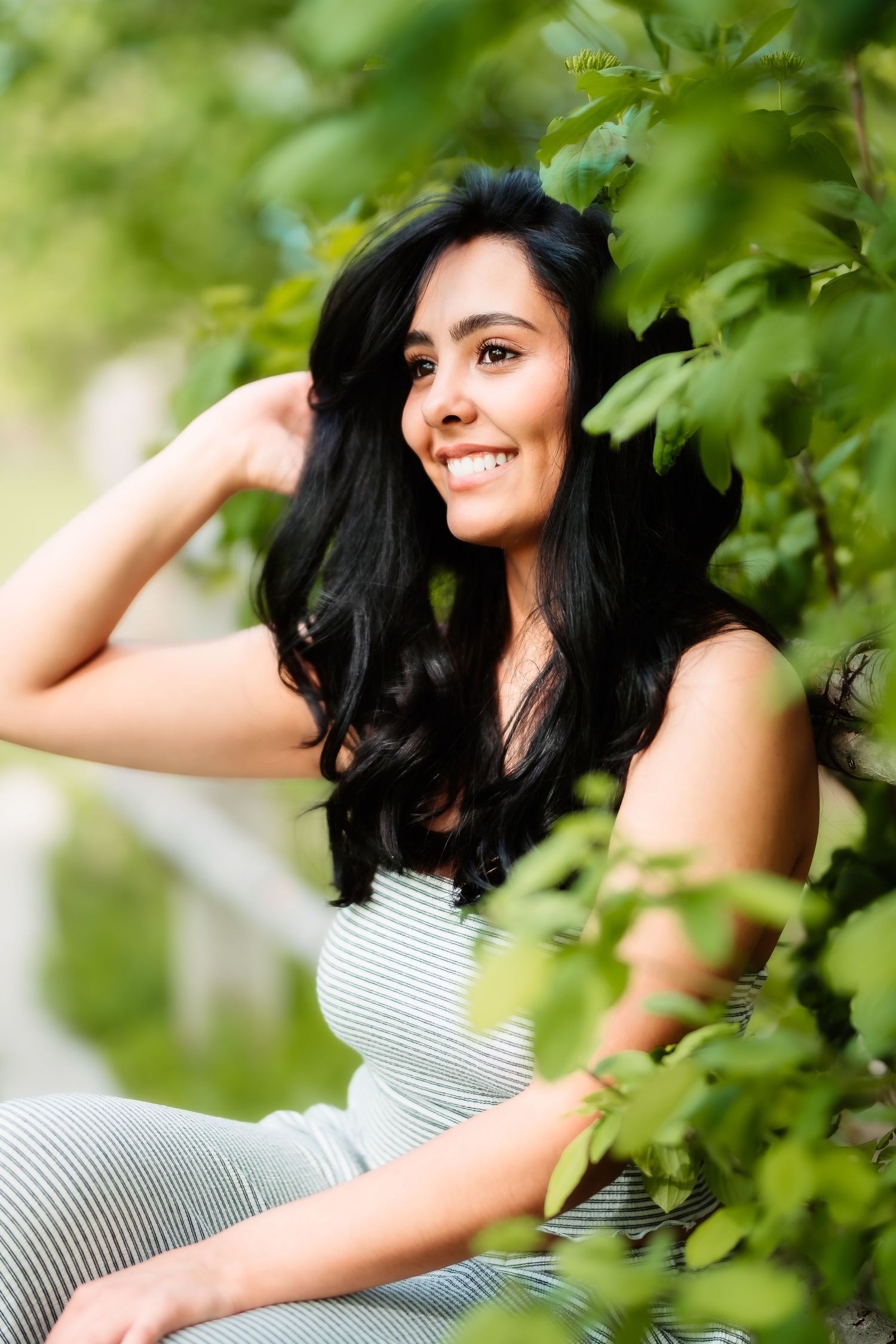 A casual outdoor portrait amidst green foliage in a striped top.