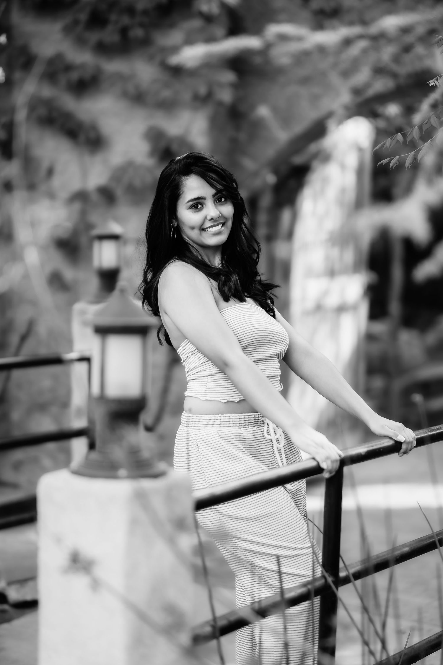 Black and white portrait of person in casual wear leaning on railing with waterfall in background.