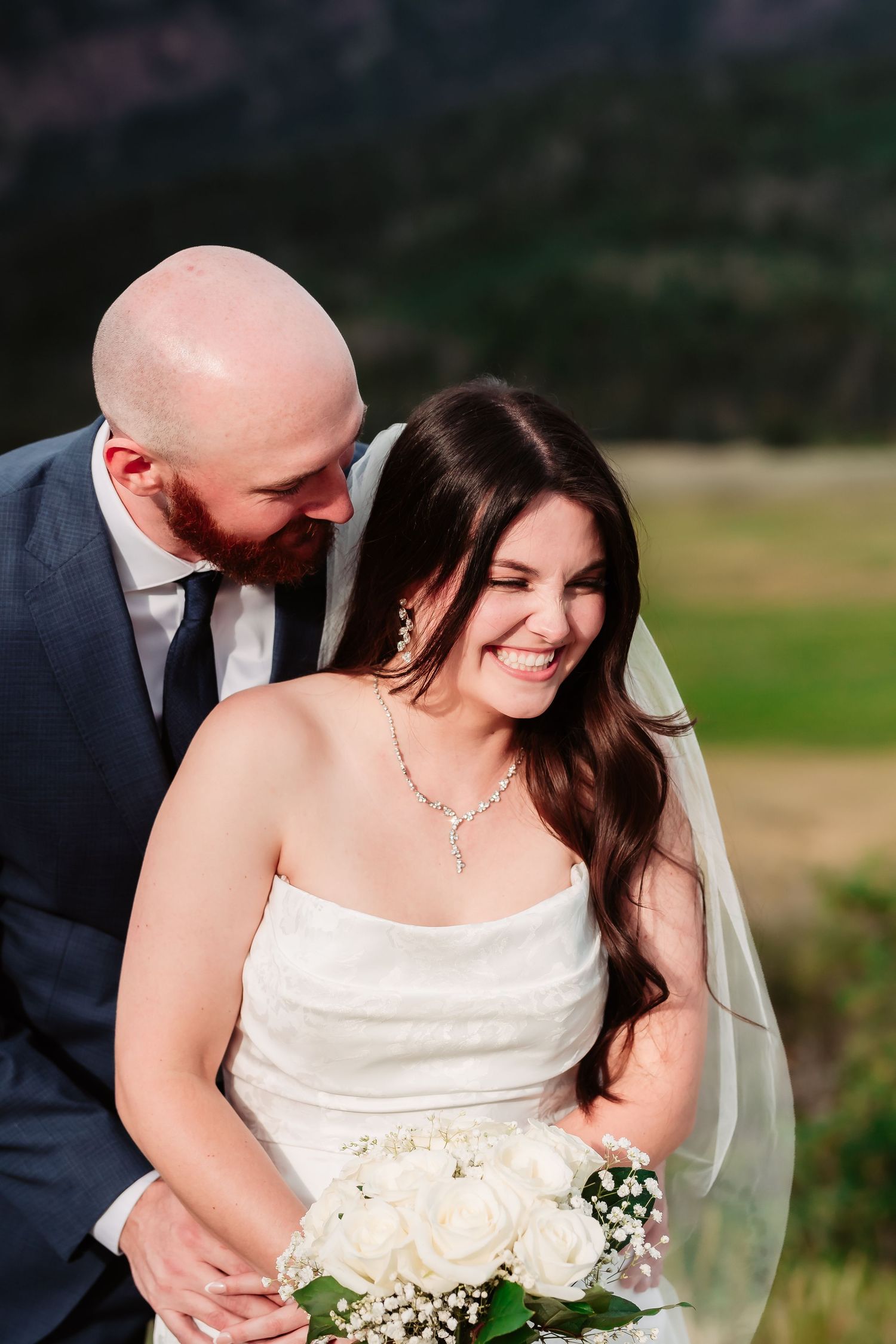 A bride holding a white bouquet smiles joyfully during an outdoor wedding photoshoot.