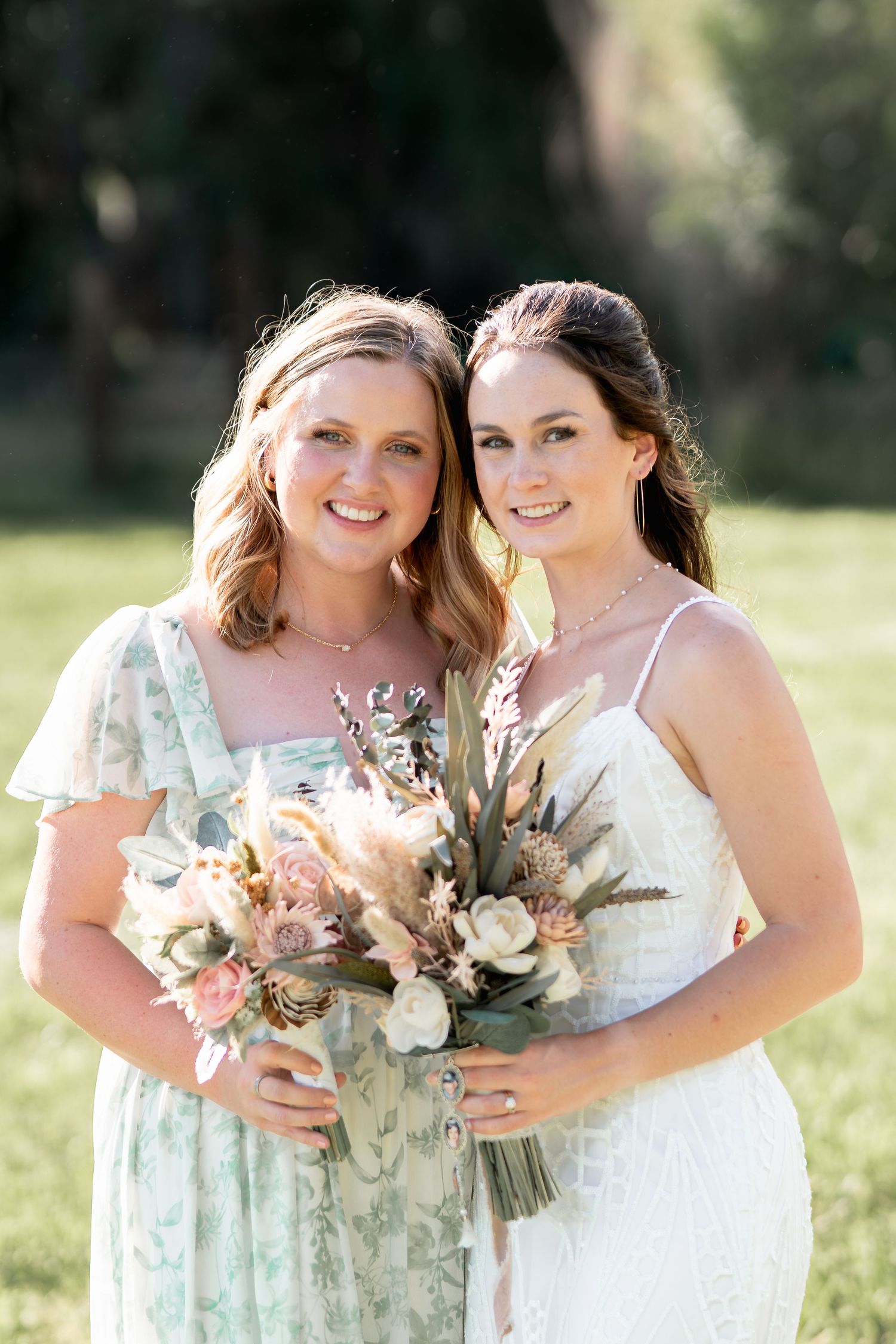 Two attendants pose with matching pastel floral bouquets in afternoon sunlight.