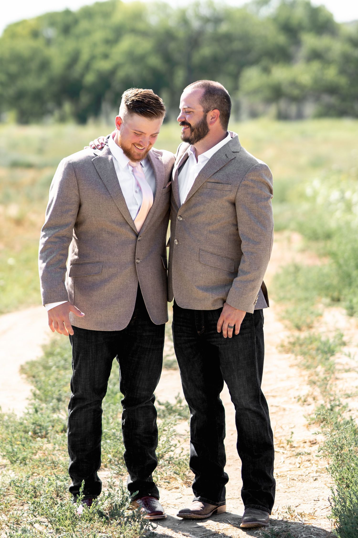 Two people wearing matching gray blazers sharing an intimate moment on a dirt path in a rural setting.