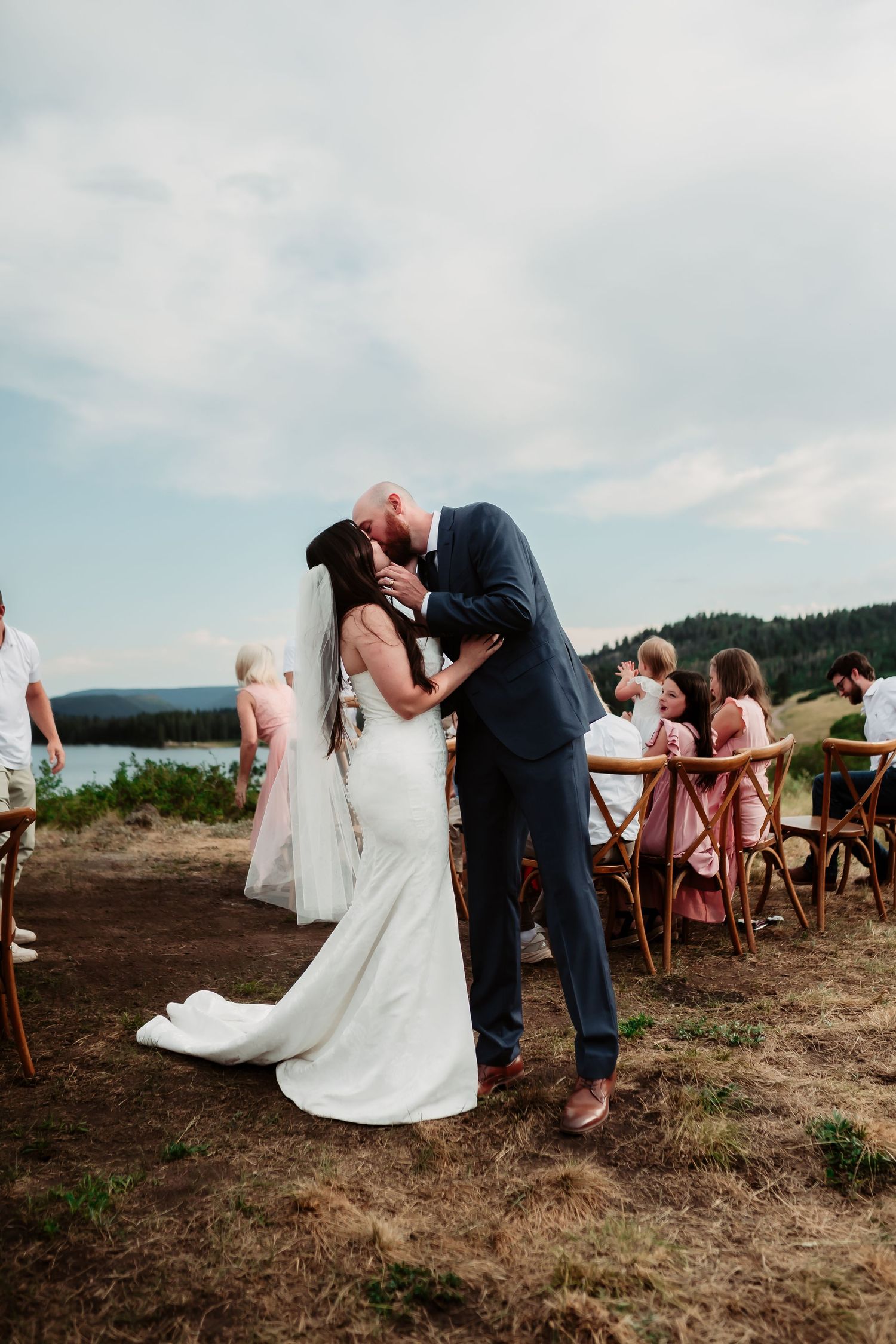 A romantic kiss during a mountaintop wedding ceremony with lake views.