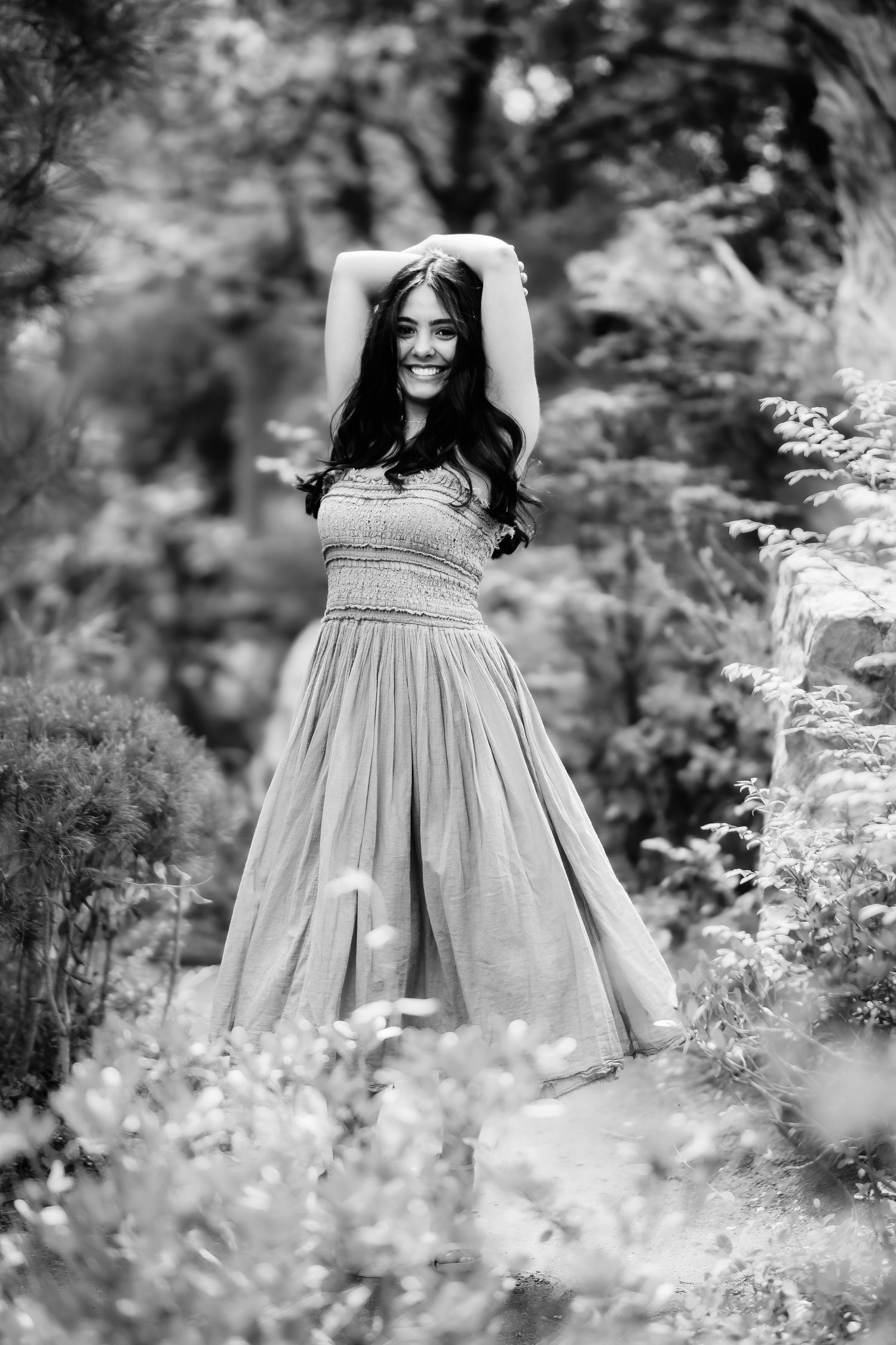 Black and white image of woman in flowing dress standing among wildflowers in garden setting.