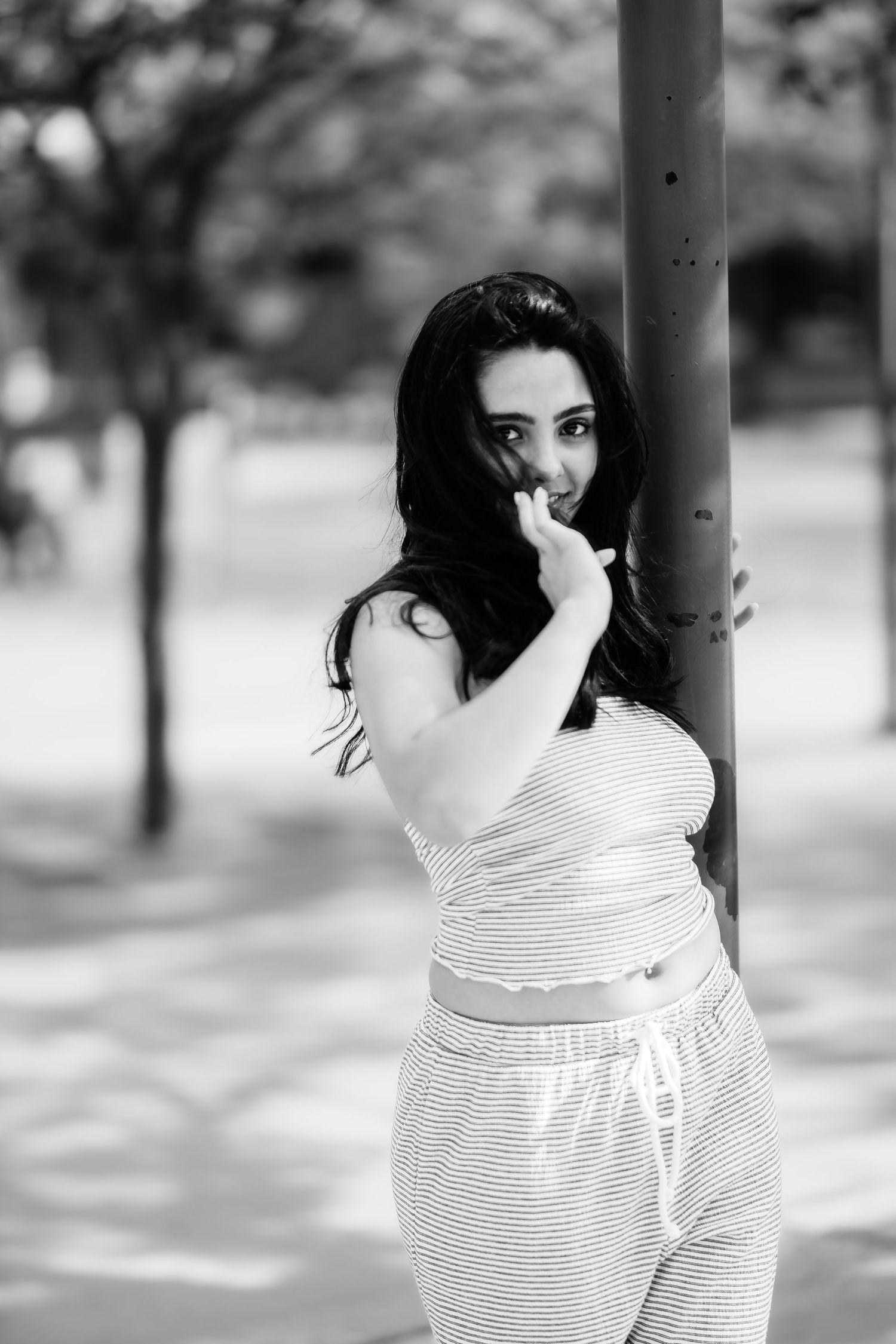 A playful black and white portrait of someone posing next to a pole in striped summer attire.