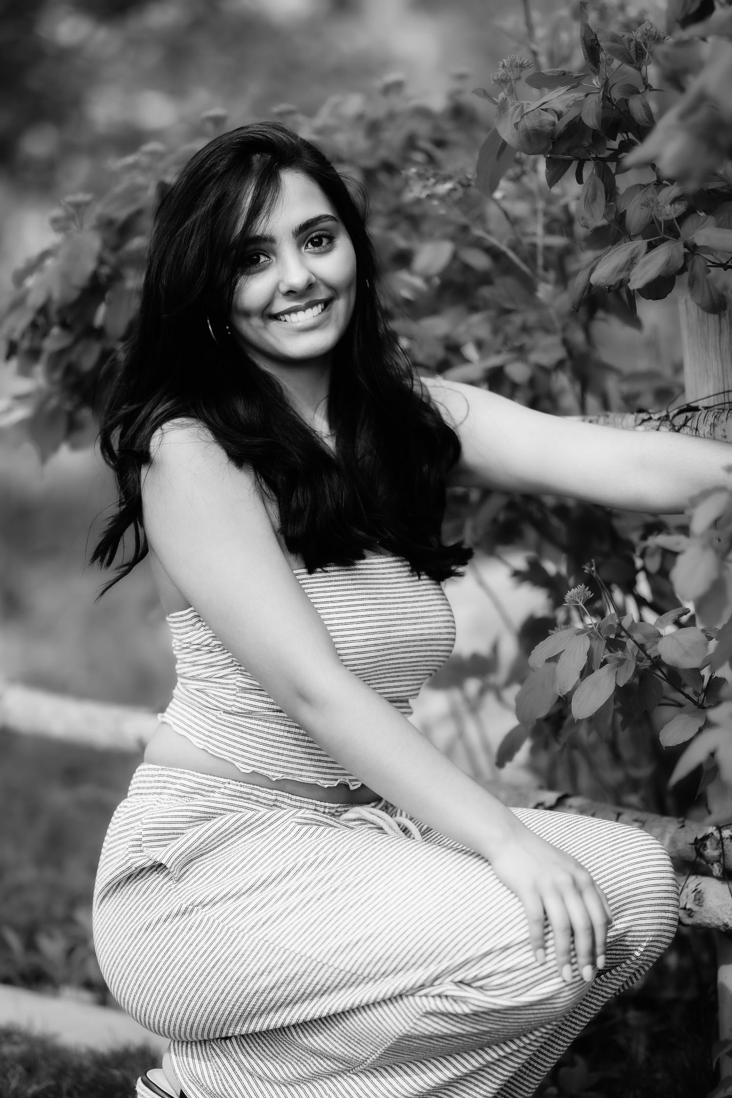 Black and white photo of woman in striped dress posing by leafy branches.
