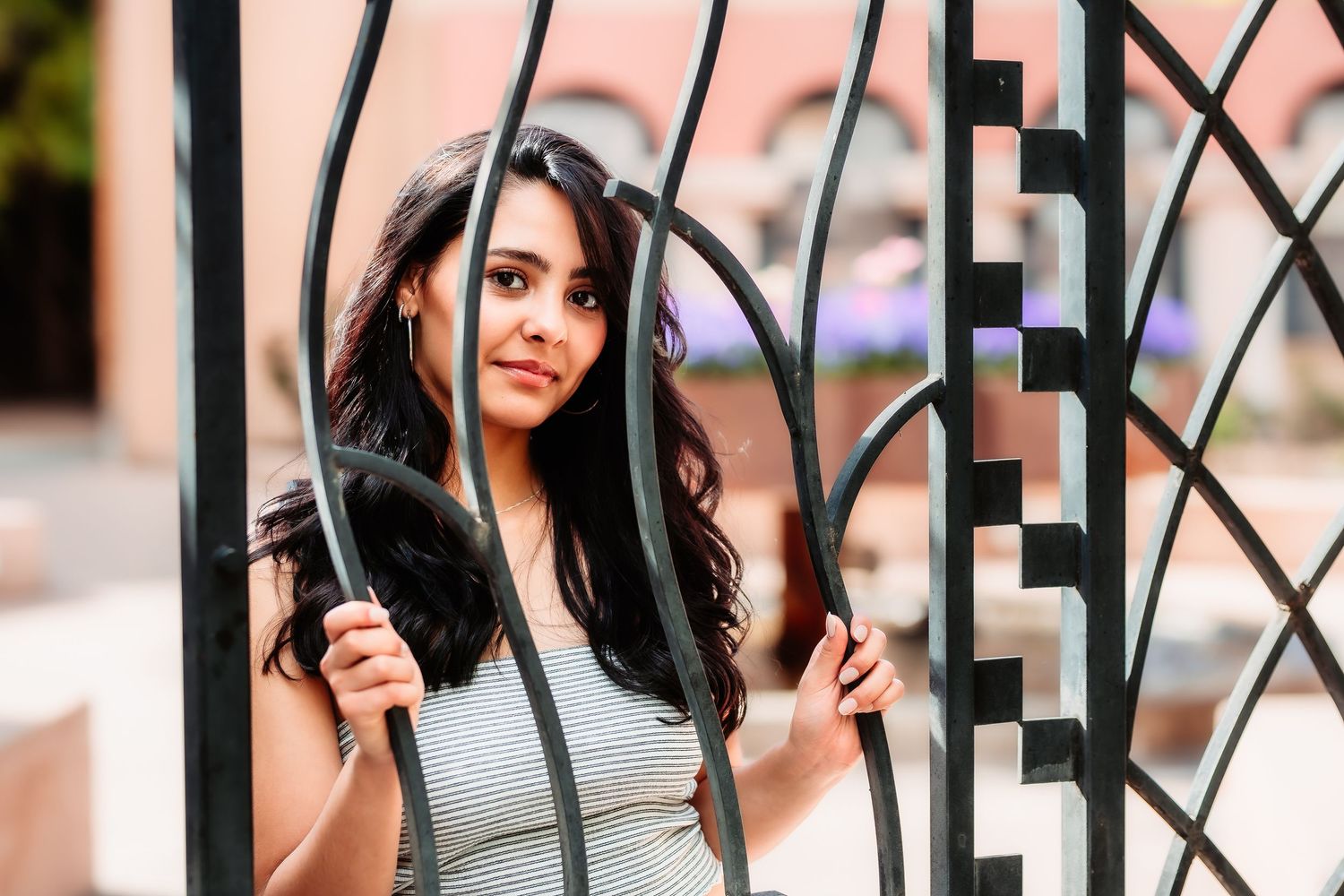 A creative portrait through decorative metal gates features someone in a gray outfit.