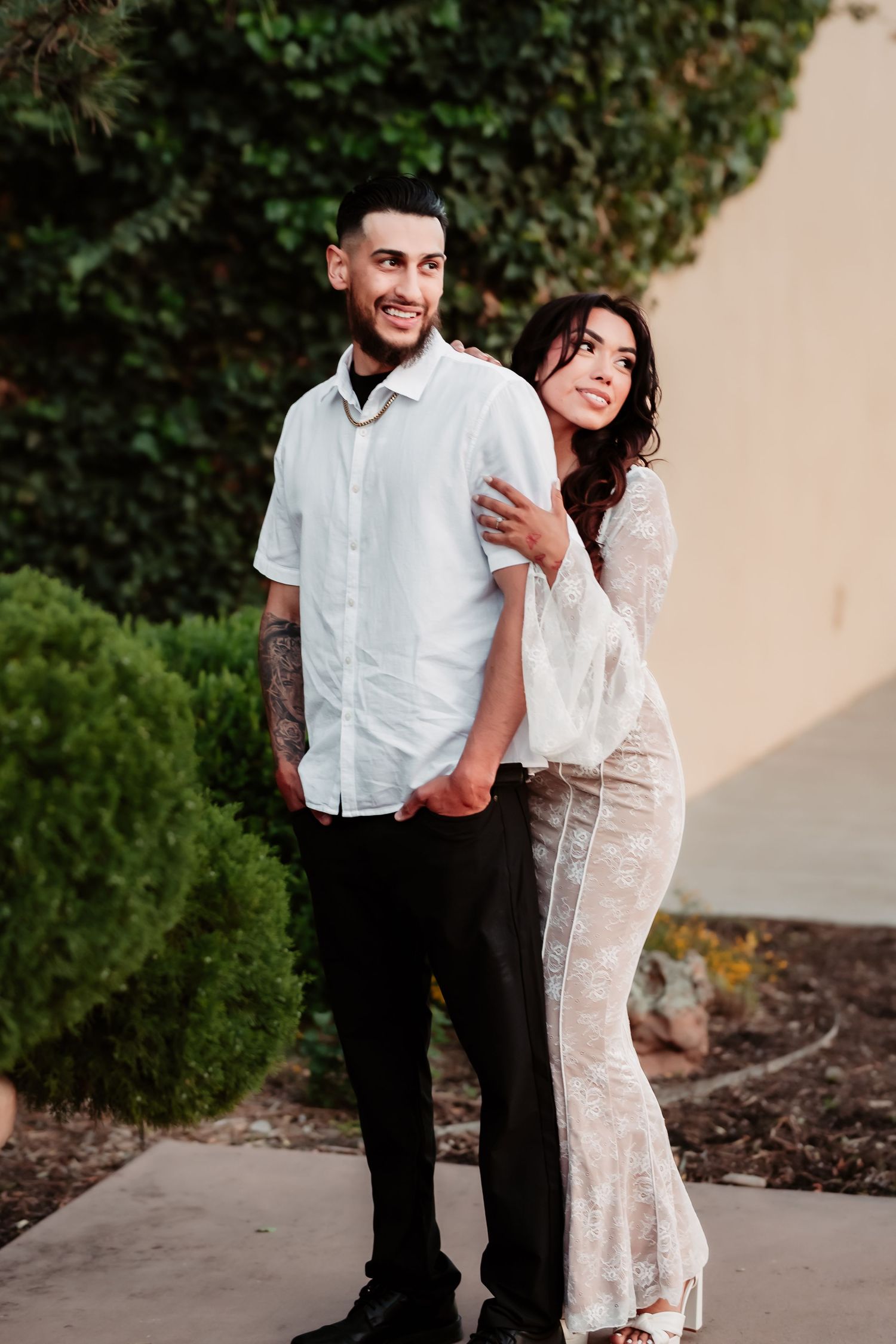 A playful outdoor couple's portrait with landscaping and stucco walls in the background.