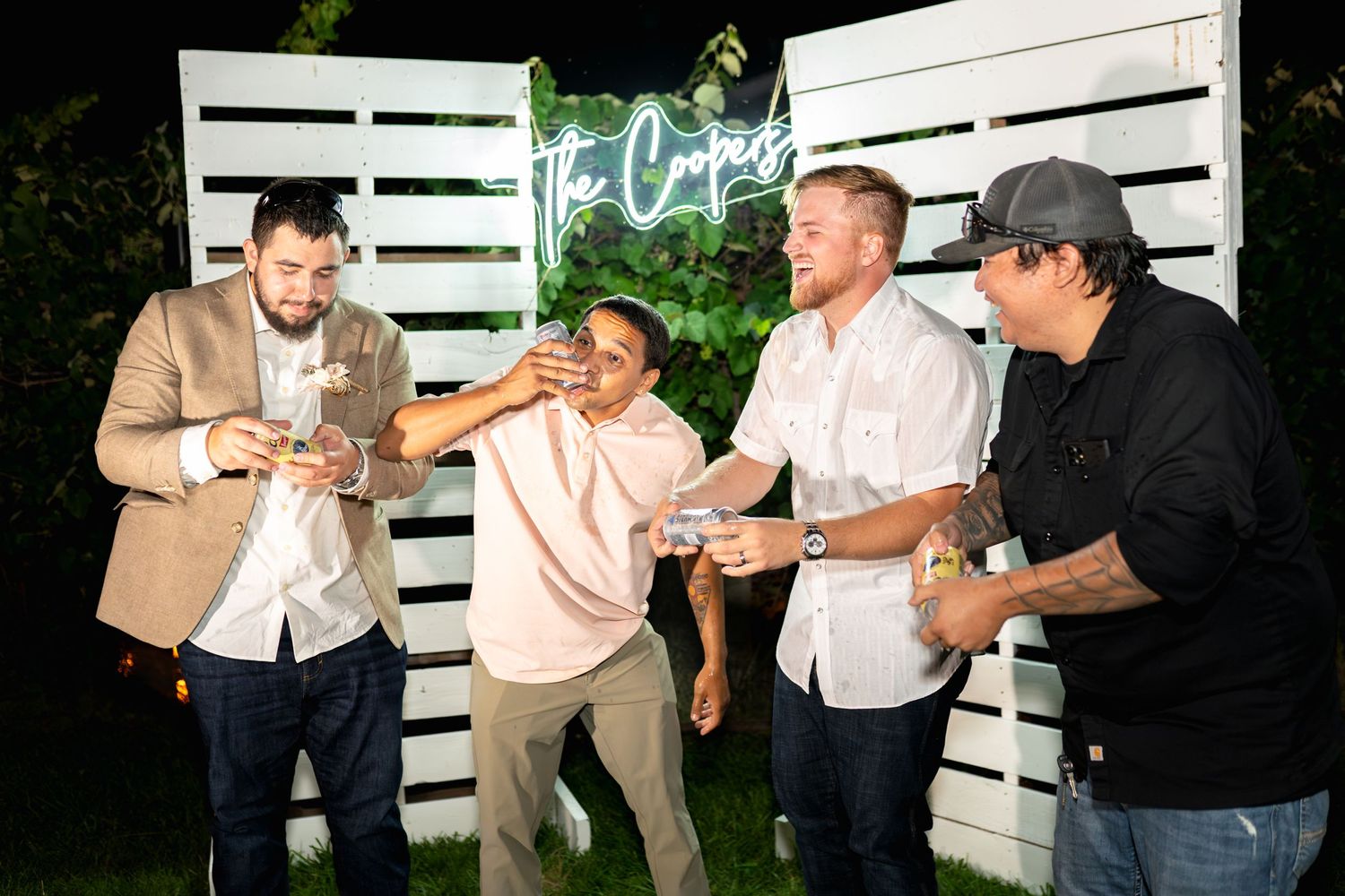Group of friends enjoying drinks and conversation against white wooden pallet backdrop.