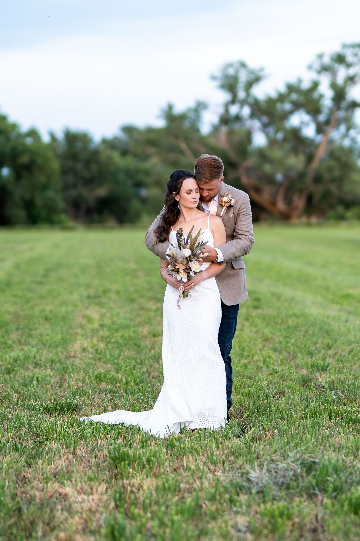 Newlyweds embrace in a romantic moment on grassy field during their wedding.