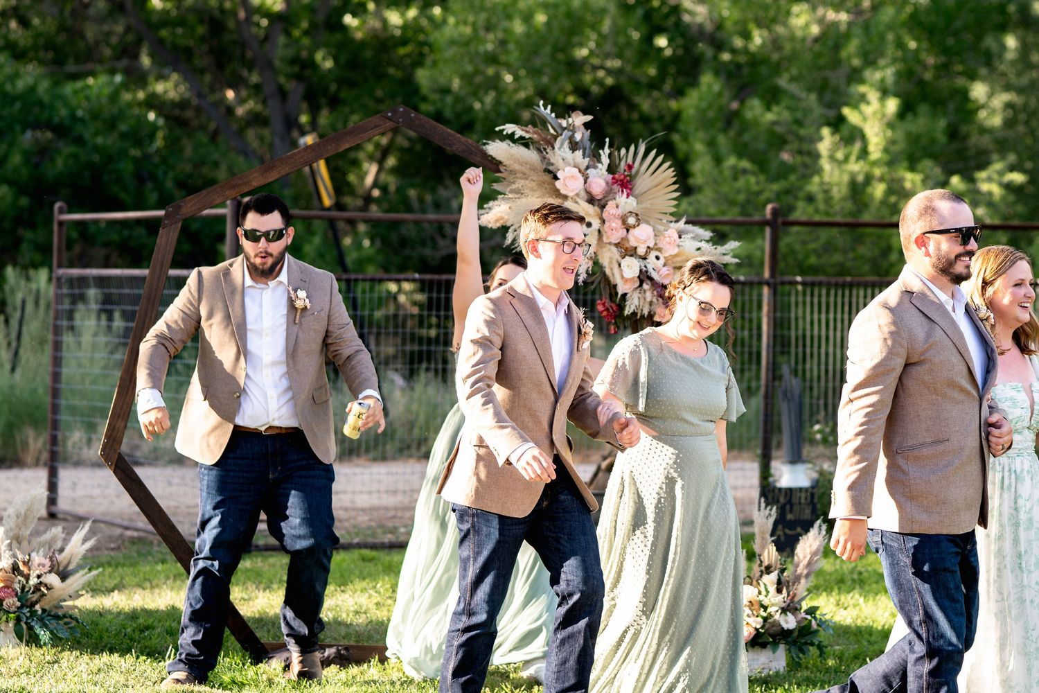 Wedding party members celebrate joyfully on a grassy lawn during outdoor festivities.