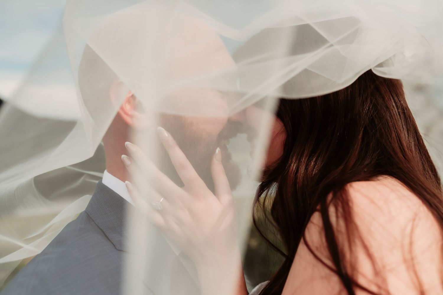 Romantic closeup of couple behind flowing white wedding veil.