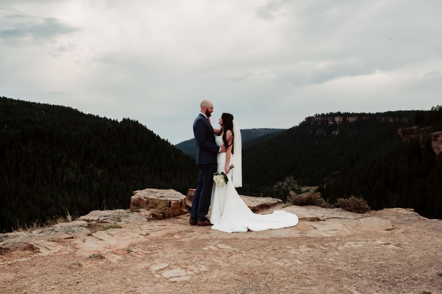 Panoramic mountain landscape wedding photos showing couple on rocky overlook with dramatic sky.