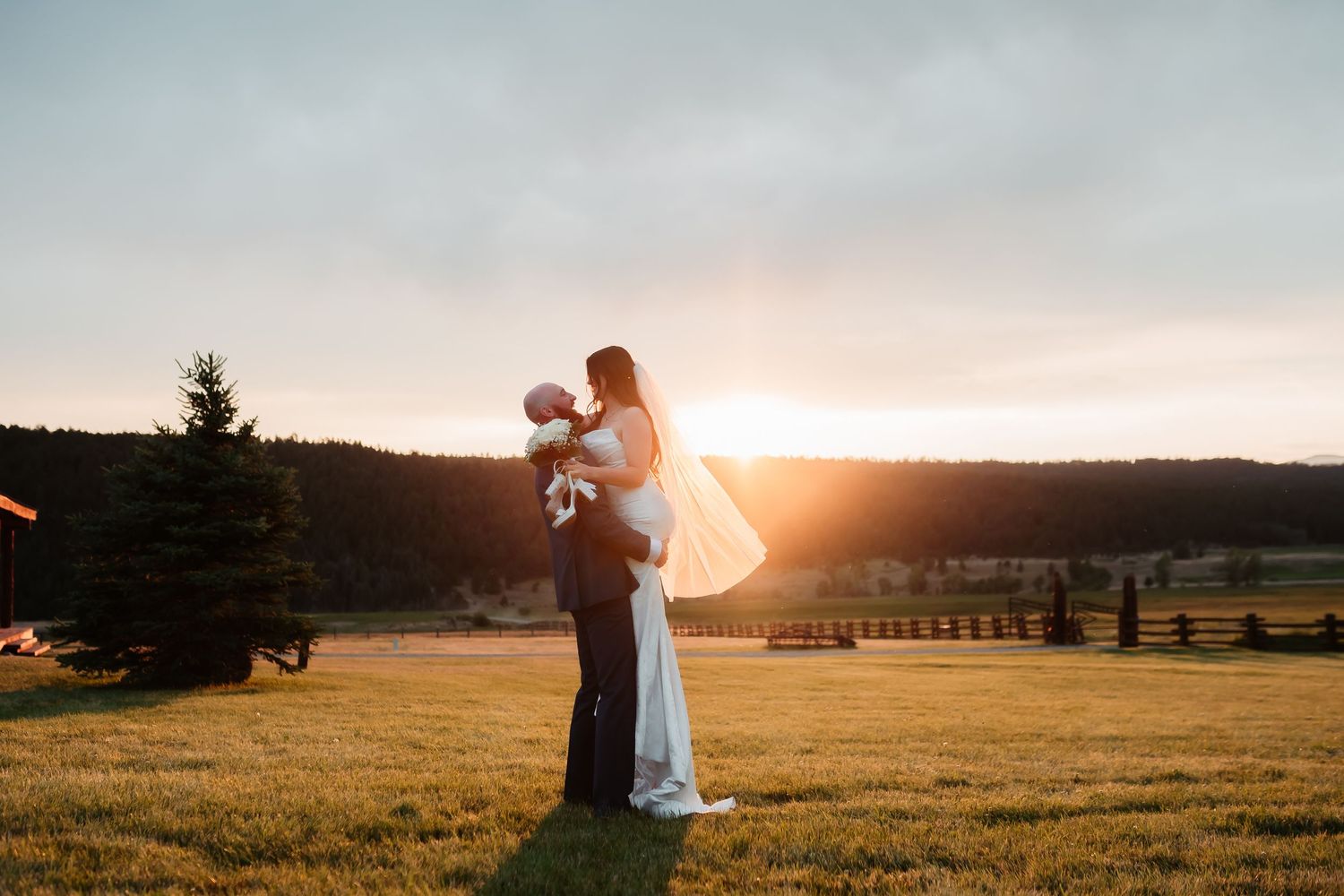 Wedding couple silhouetted against golden sunset in open field.