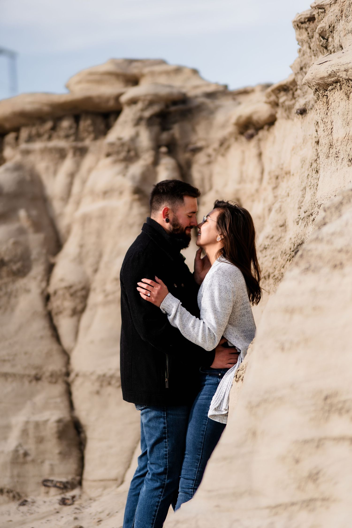Romantic couple embracing against dramatic rock formations in a desert landscape at sunset.