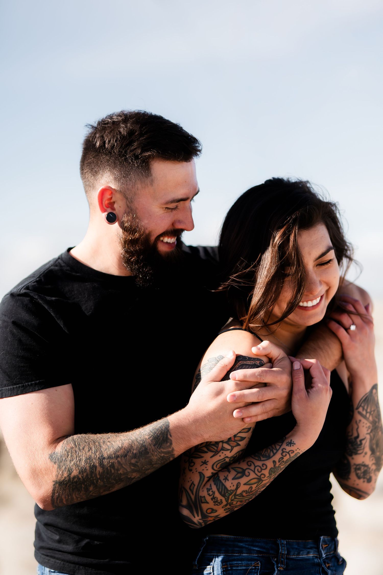 Tattooed couple laughing together on a sunny day outdoors.